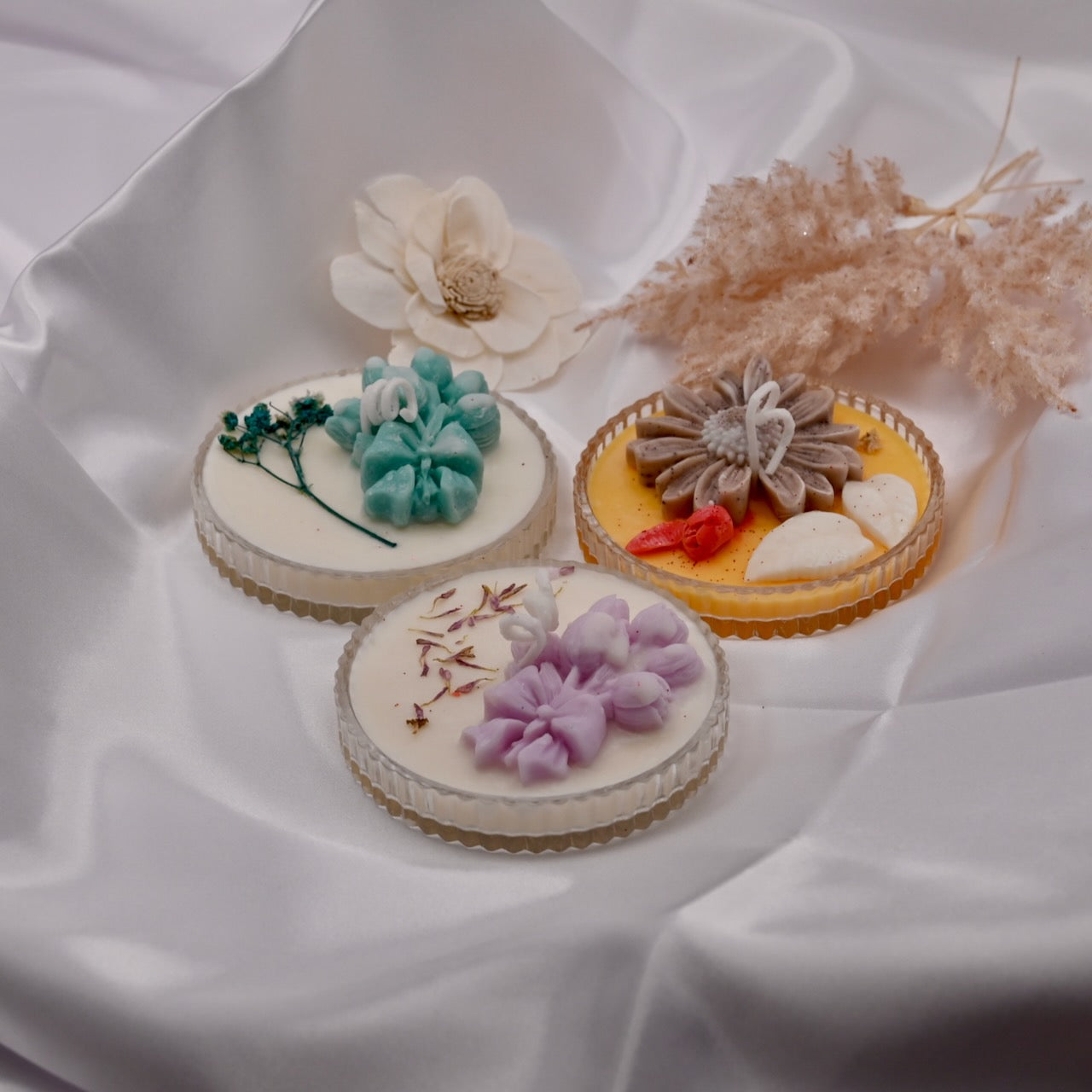Three small decorative candles with floral designs on a white fabric background