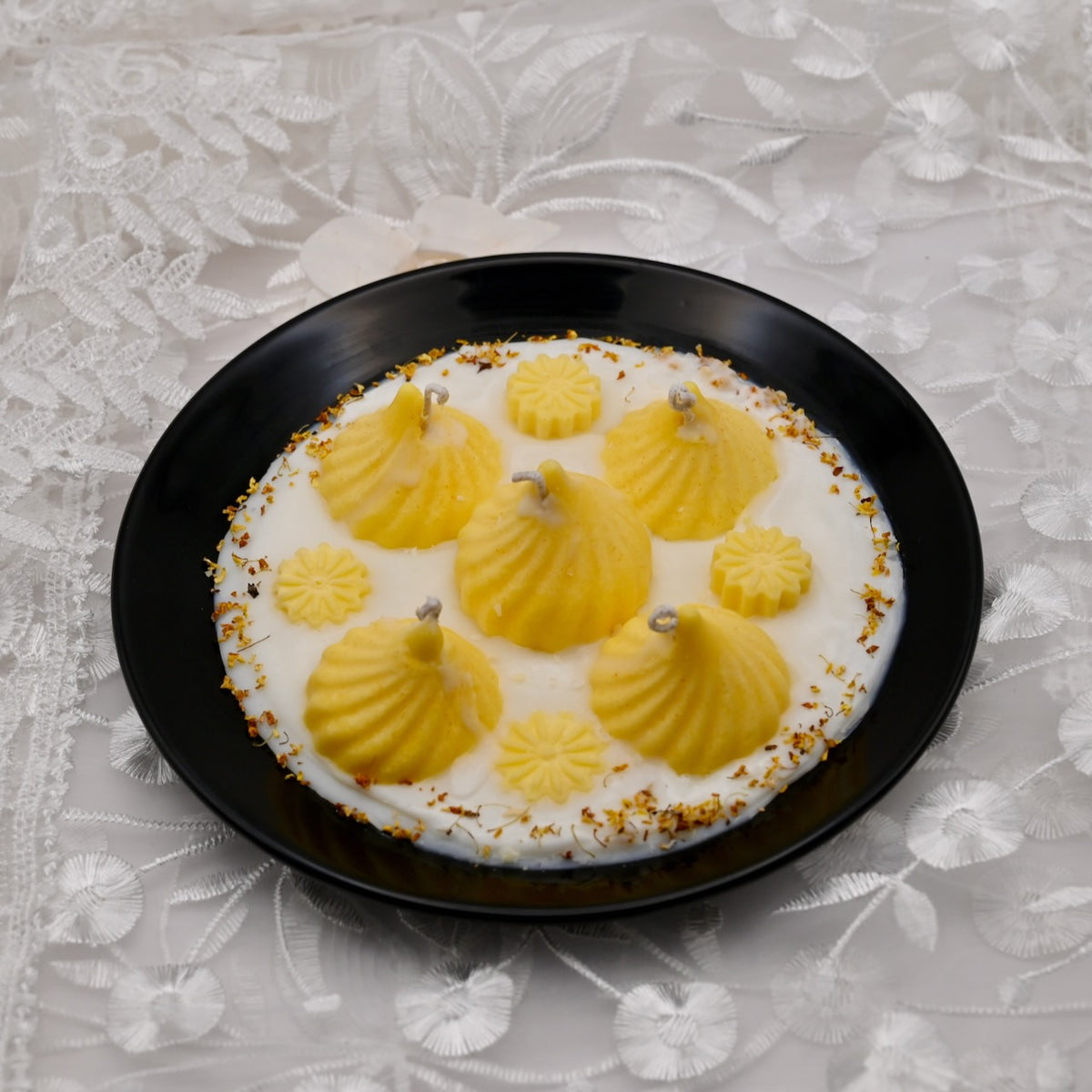 Decorative dish with yellow dessert on a black plate against a textured white background. Indian sweet - modak.