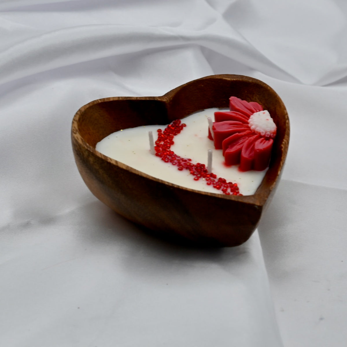 Forever Yours three-wick soy wax candle in a heart-shaped wooden bowl, decorated with a red wax flower and red beads on white satin.