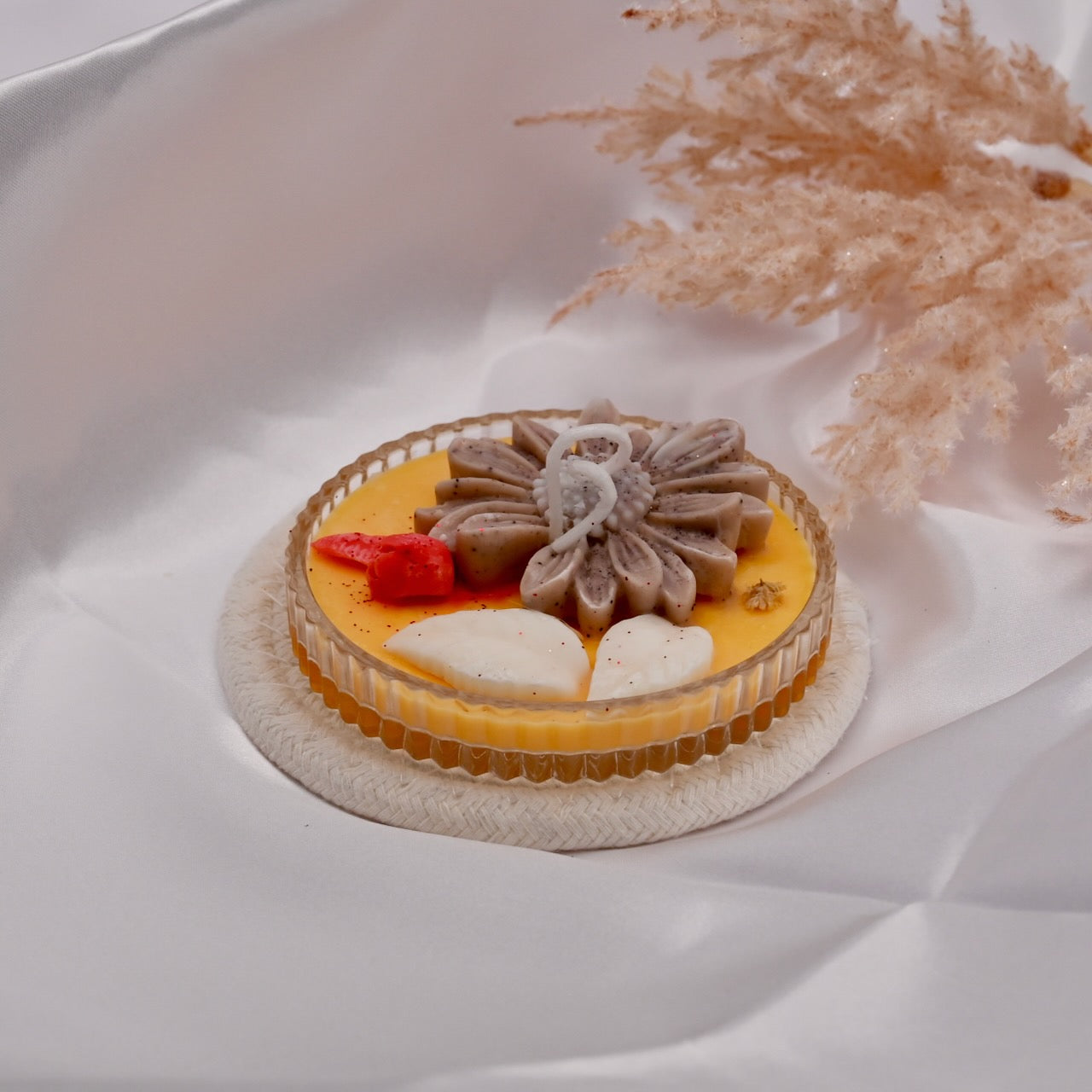 Small candle with floral decoration on a white surface with dried flowers in the background