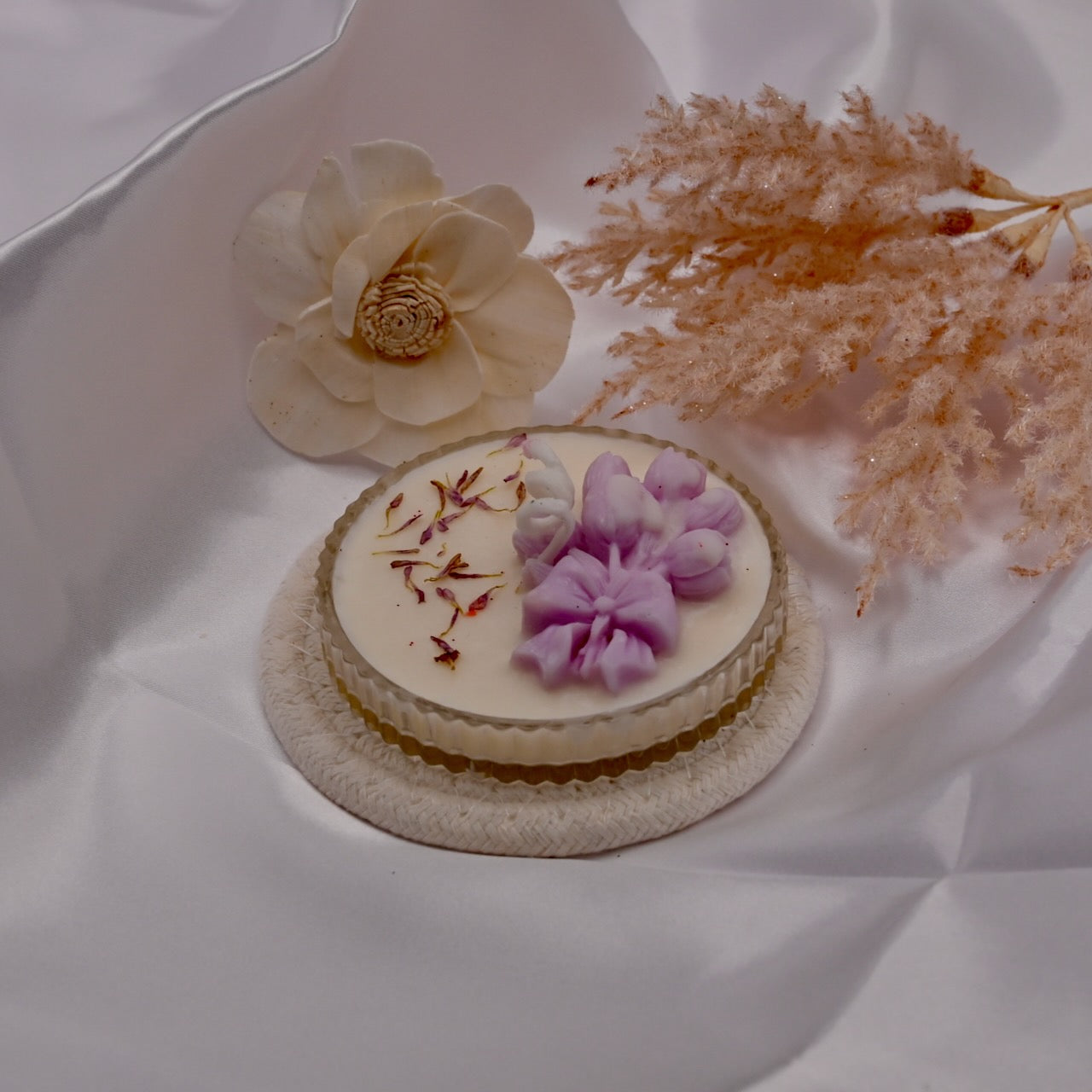 Small decorative candle with floral elements on a white fabric background