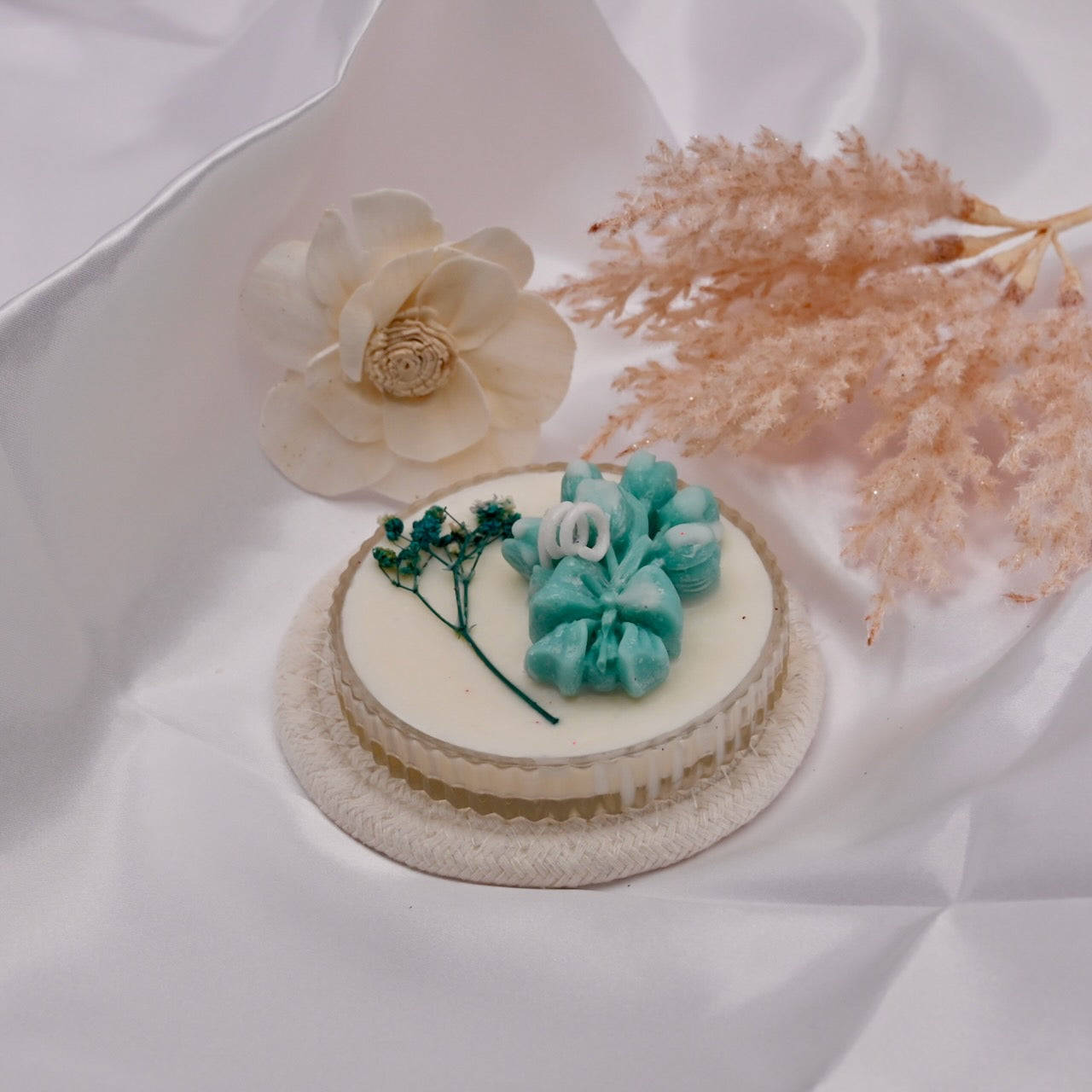 Small round candle with decorative flowers on a white fabric background