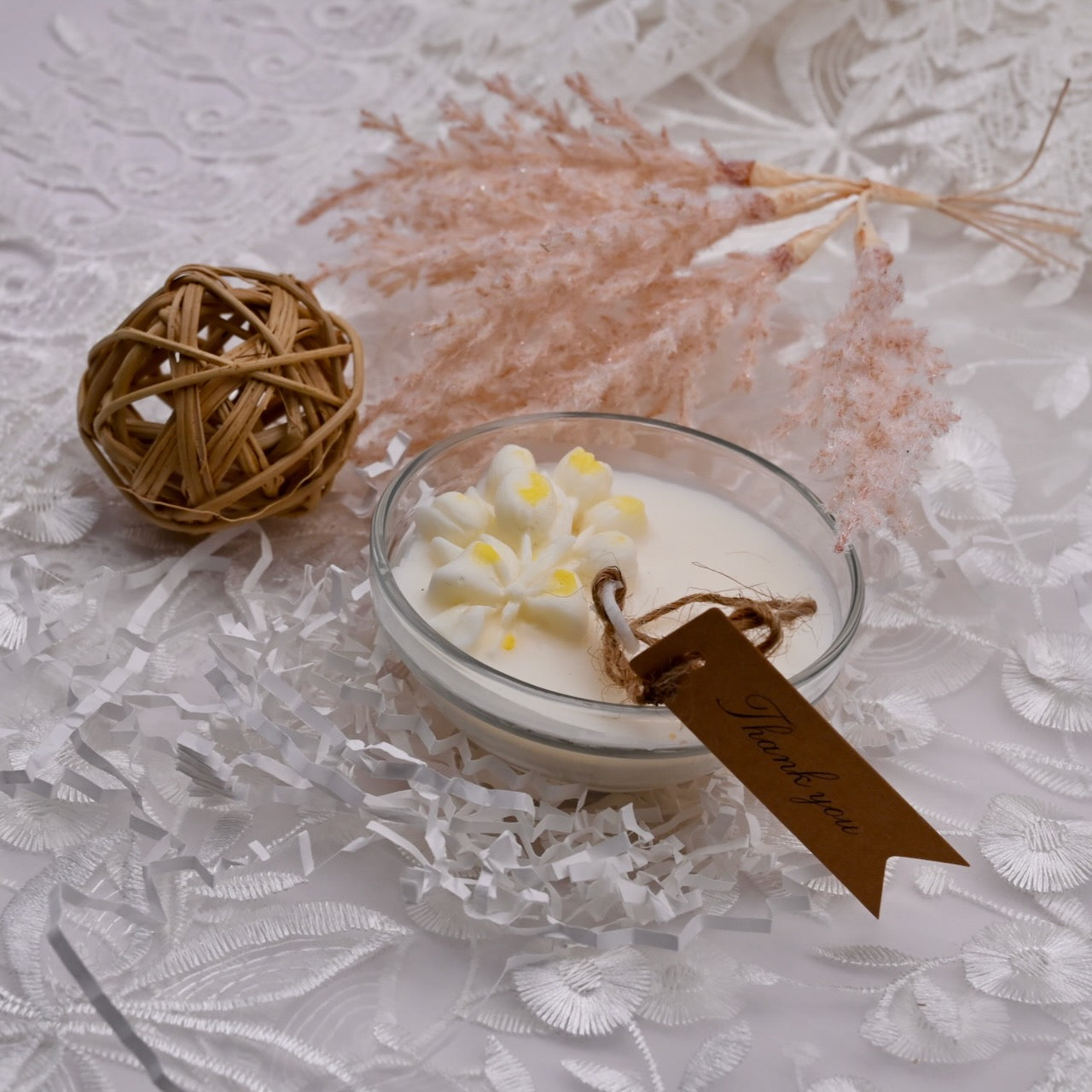 Candle in a glass jar with a decorative tag on a textured white surface