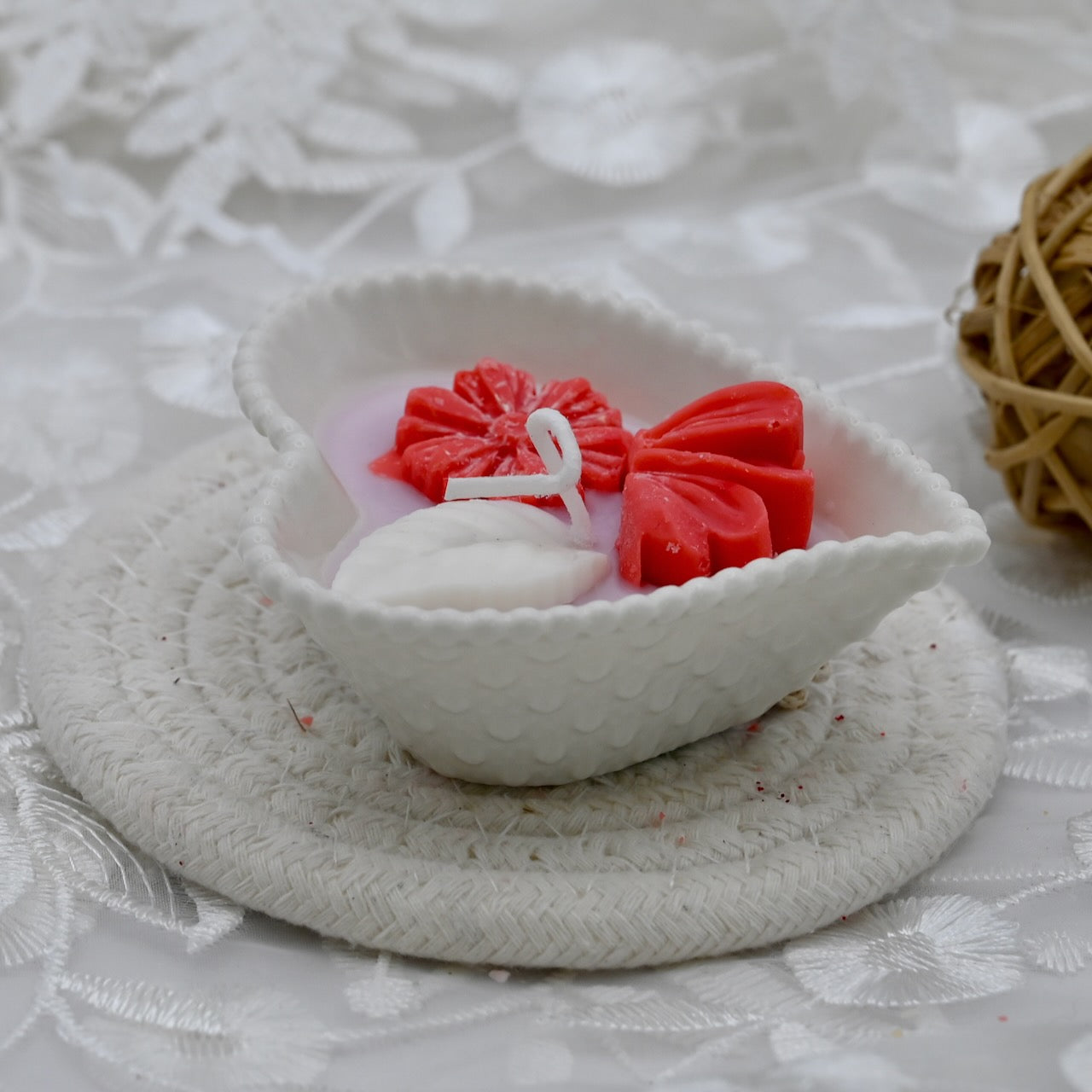 White shell with a red flower and white candle on a textured white surface
