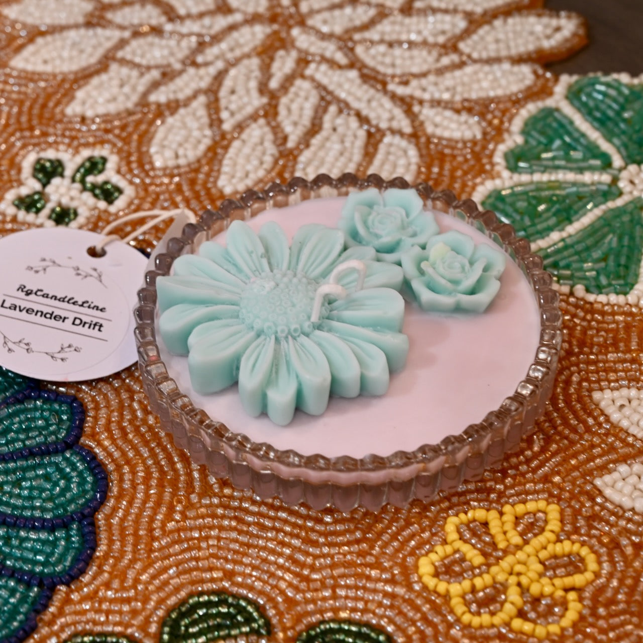 Two light blue floral decorative candles on a pink dish with a decorative background