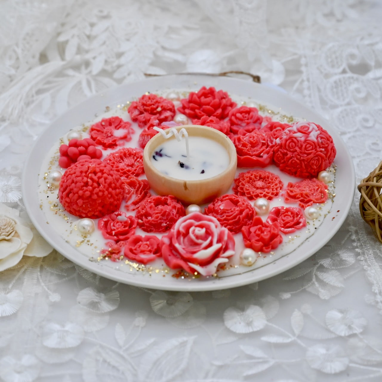 Decorative plate with red floral designs and a small candle on a textured white surface. Diwali decorative plate.