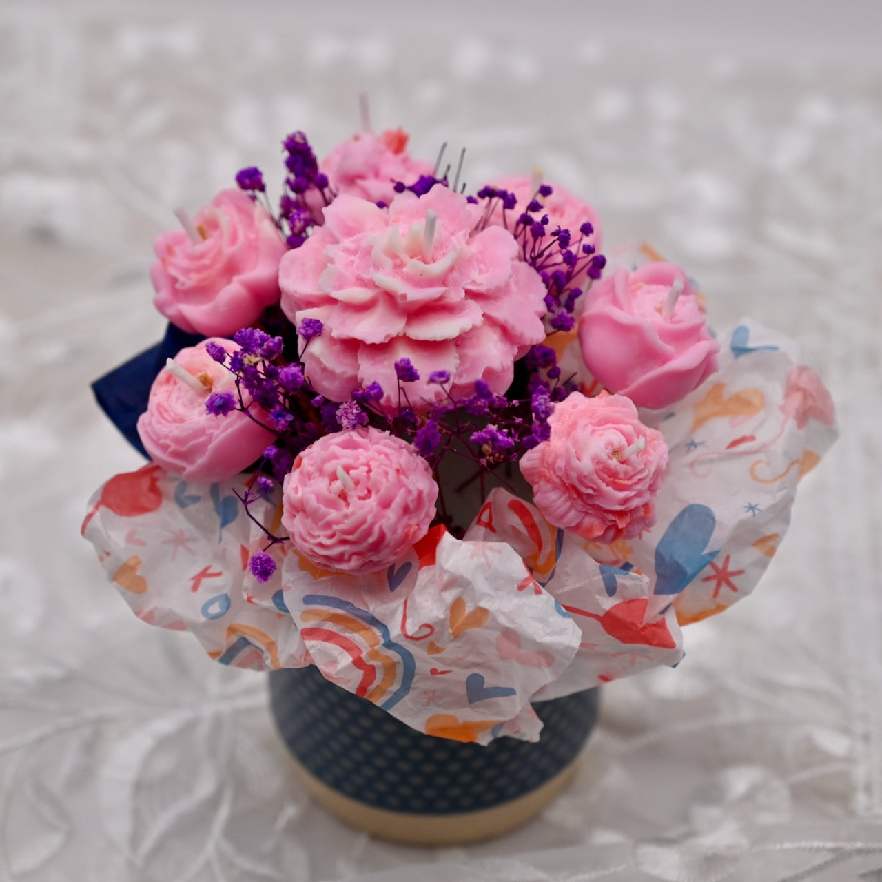 Bouquet of pink and purple flowers in a colorful paper wrap on a textured surface.