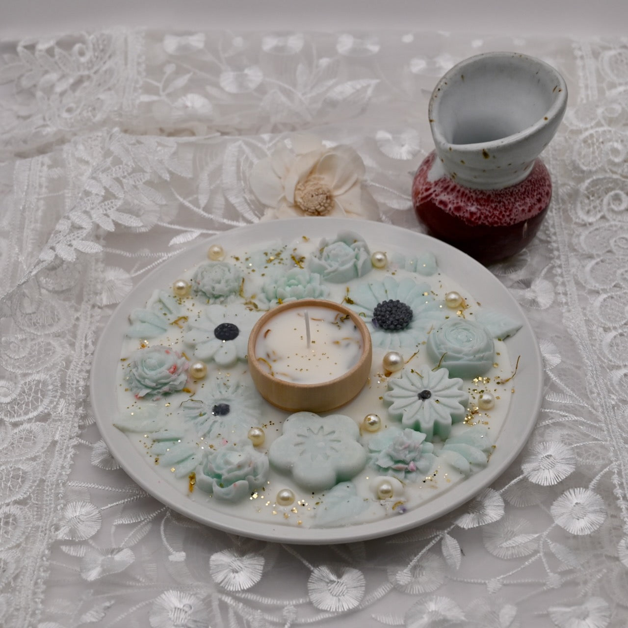 Decorative plate with floral designs, a candle, and small decorative items on a lace tablecloth.  Diwali decorative plate.