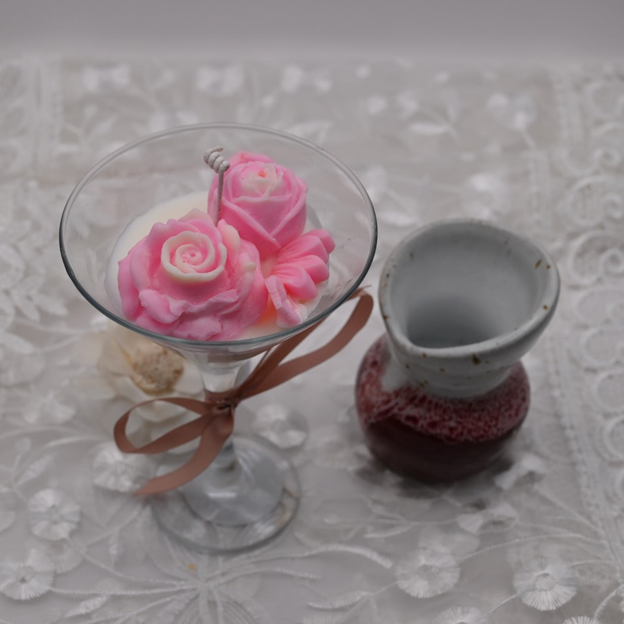 Decorative pink rose-shaped candles in a glass holder on a textured surface.