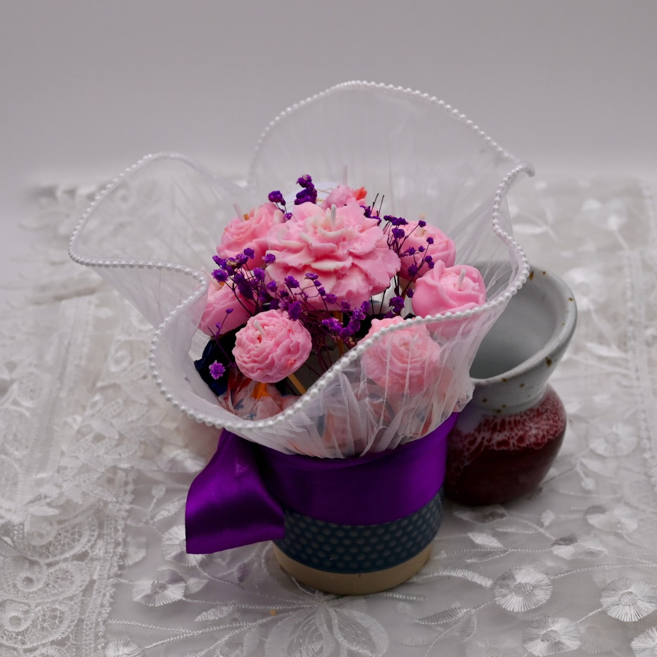 Decorative flower arrangement in a pot with a purple ribbon on a lace tablecloth