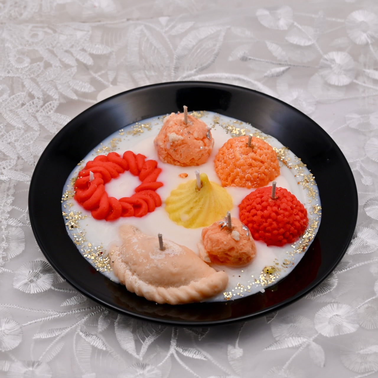 Decorative candles shaped like indian sweets - imarti, jalebi, laddu, modak, gujiya on a black plate with a white background.  Diwali decorative plate.