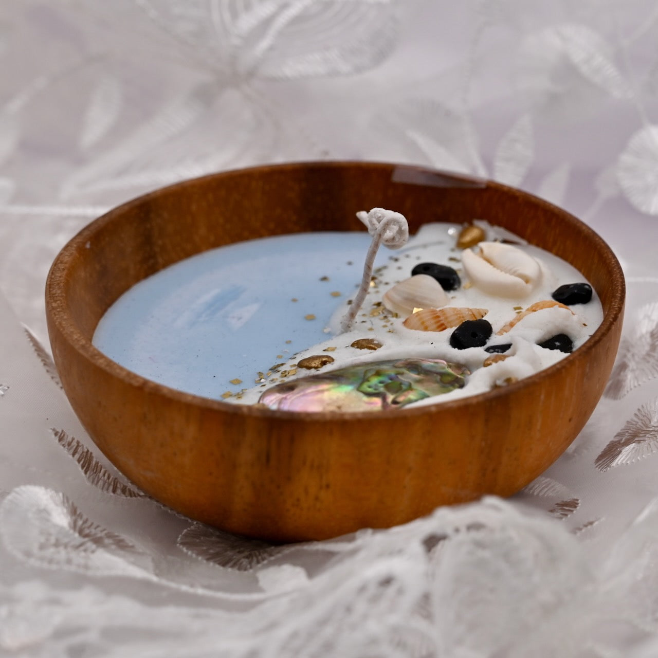 Wooden bowl with a candle inside, featuring seashells and a decorative design on a textured white background.