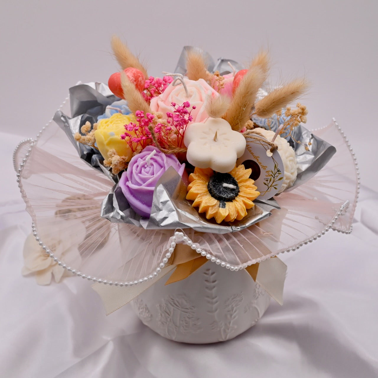 Decorative arrangement of flowers and candles on a white stand with a light gray background