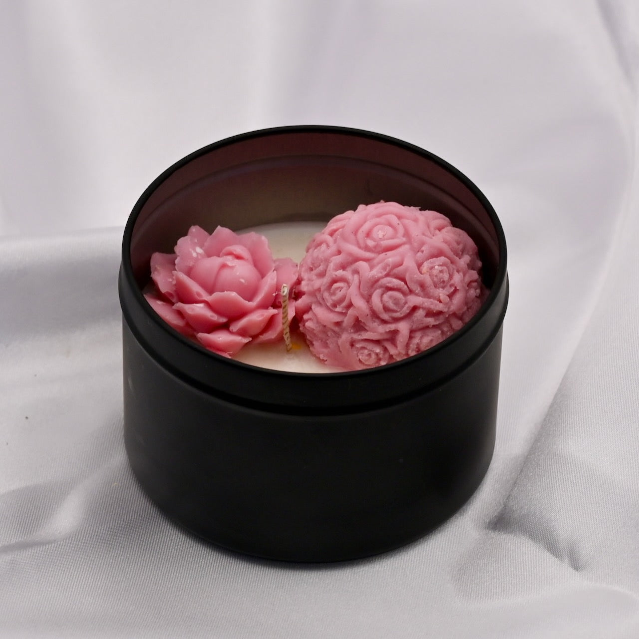 Black container with a candle and pink floral designs on a white background