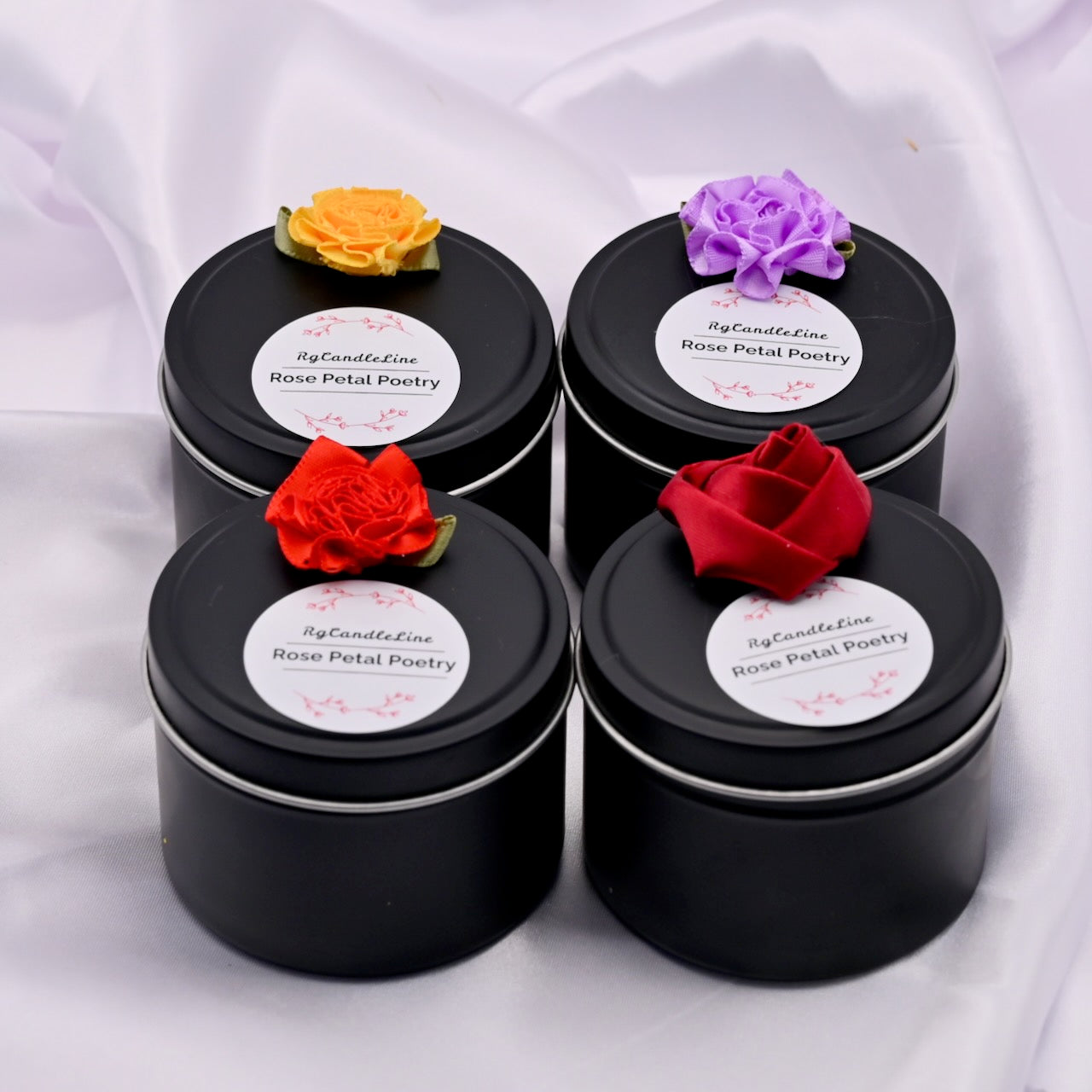 Four black tins with rose petal decorations on a white background