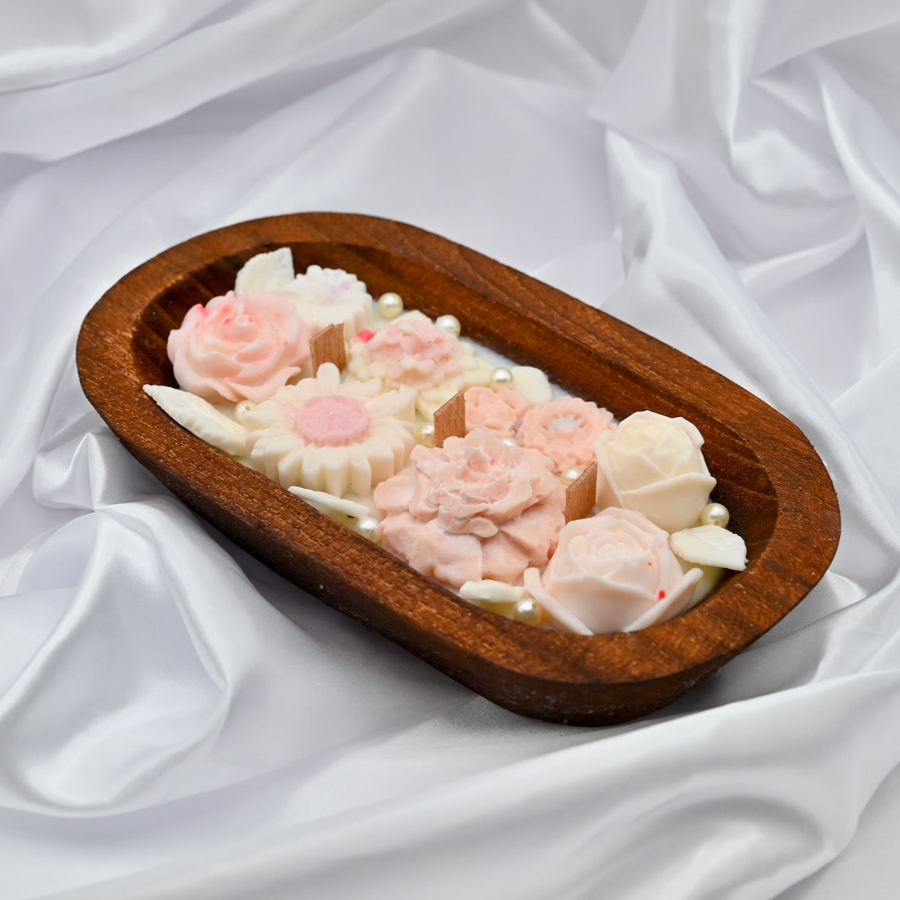 Wooden dish with floral-shaped soap bars on a white fabric background
