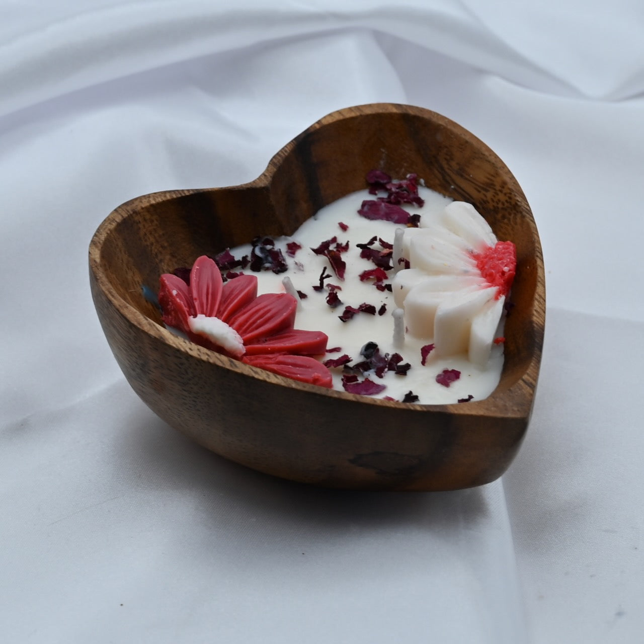 Wooden heart-shaped bowl with a white candle and decorative flowers on a white fabric background