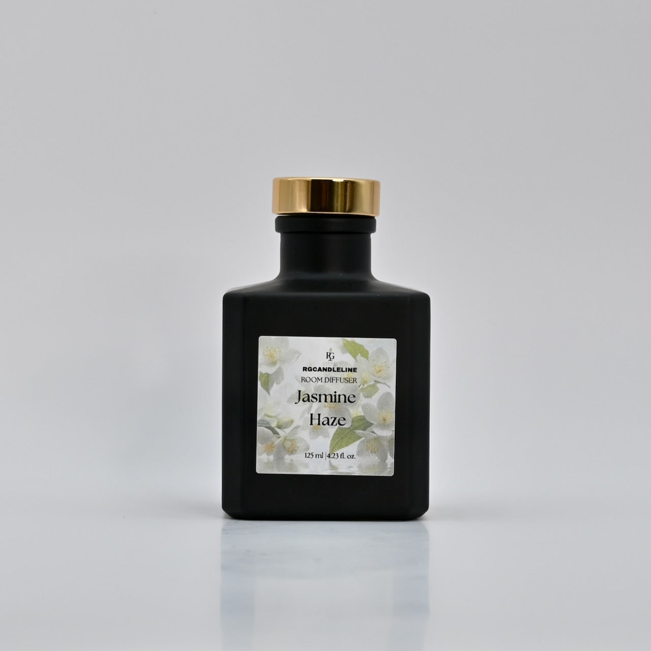 Black bottle of 'Jasmine Haze' perfume with a gold cap on a gray background