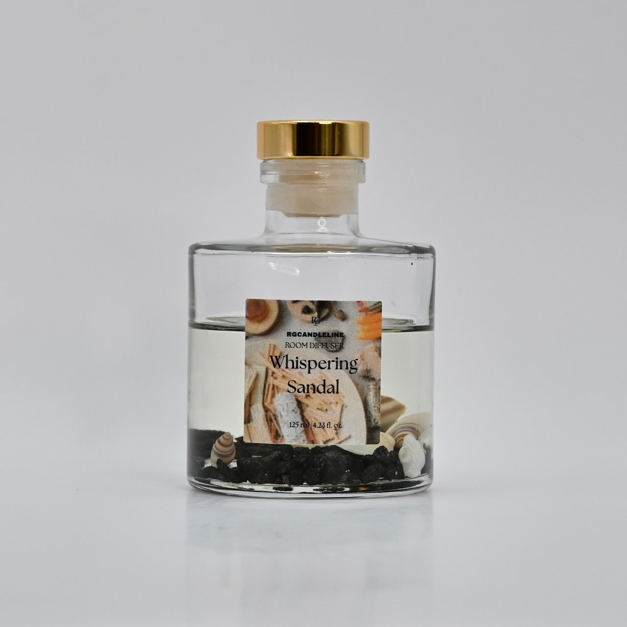 Clear glass bottle with a gold cap and 'Whispering Sandal' label on a white background