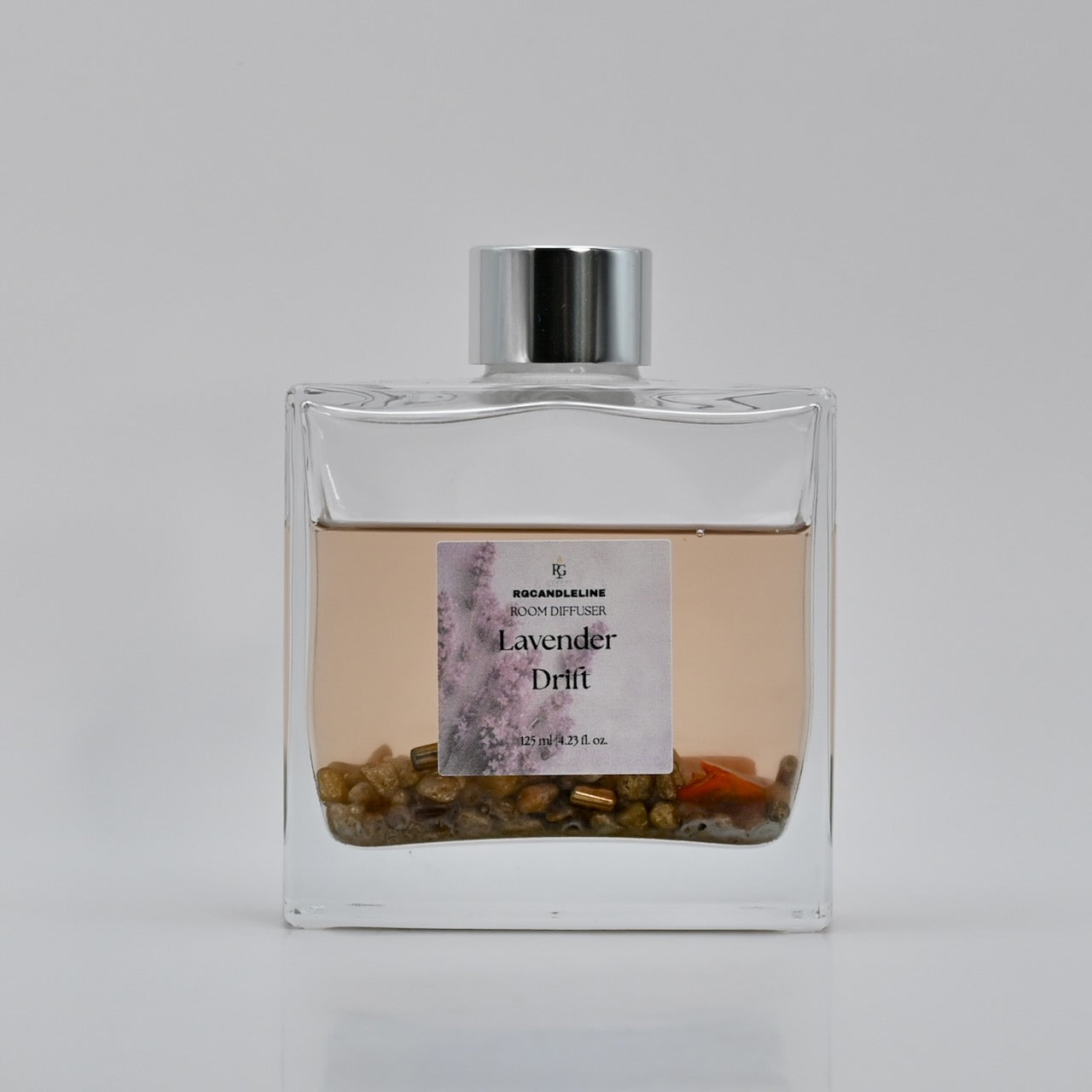 Clear glass diffuser bottle with a silver cap on a light gray background