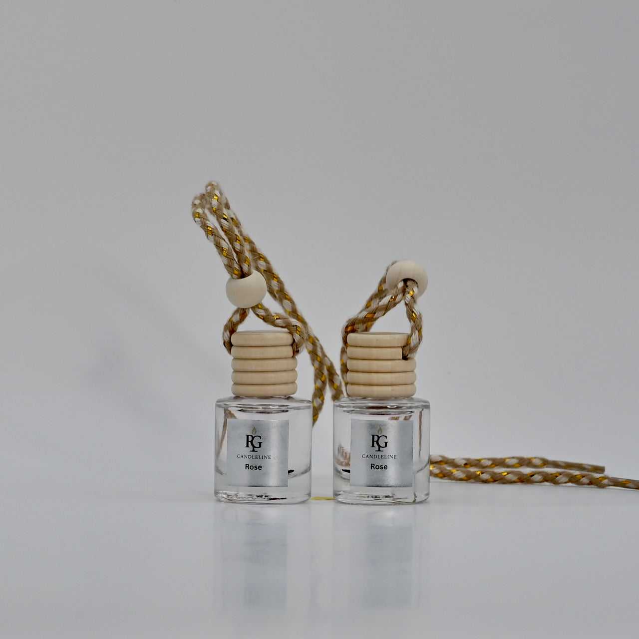 Two clear perfume bottles with wooden caps on a gold chain against a gray background