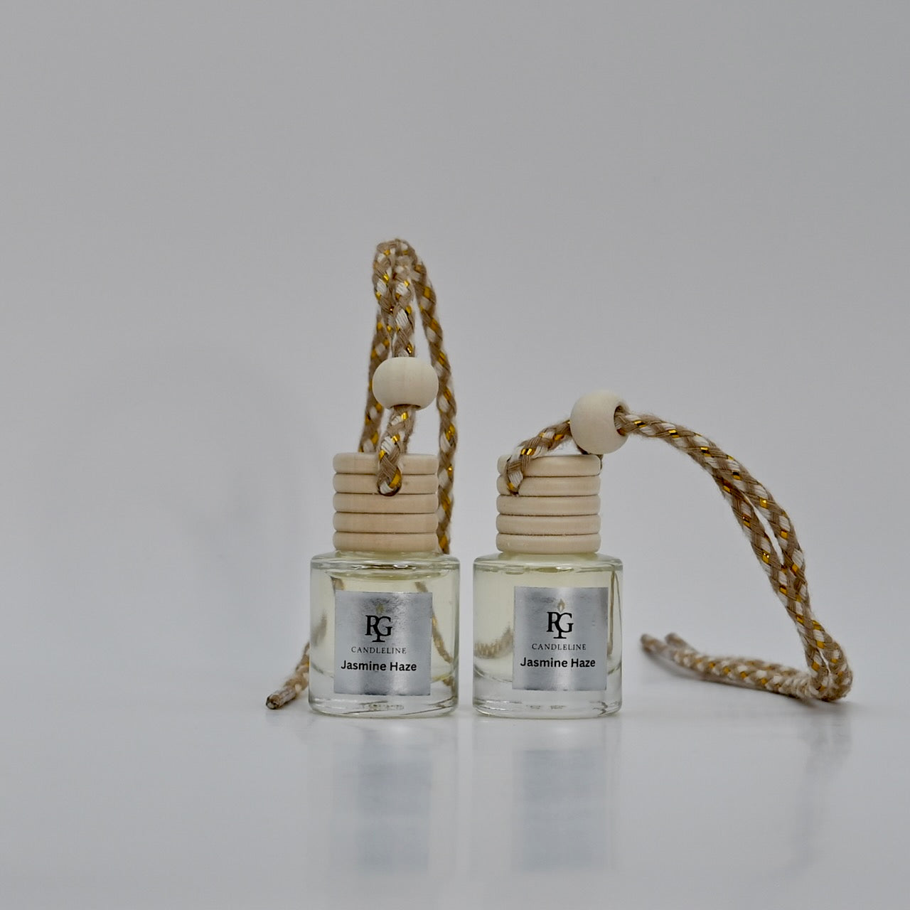 Two small glass bottles with wooden caps and gold braided strings on a light gray background.