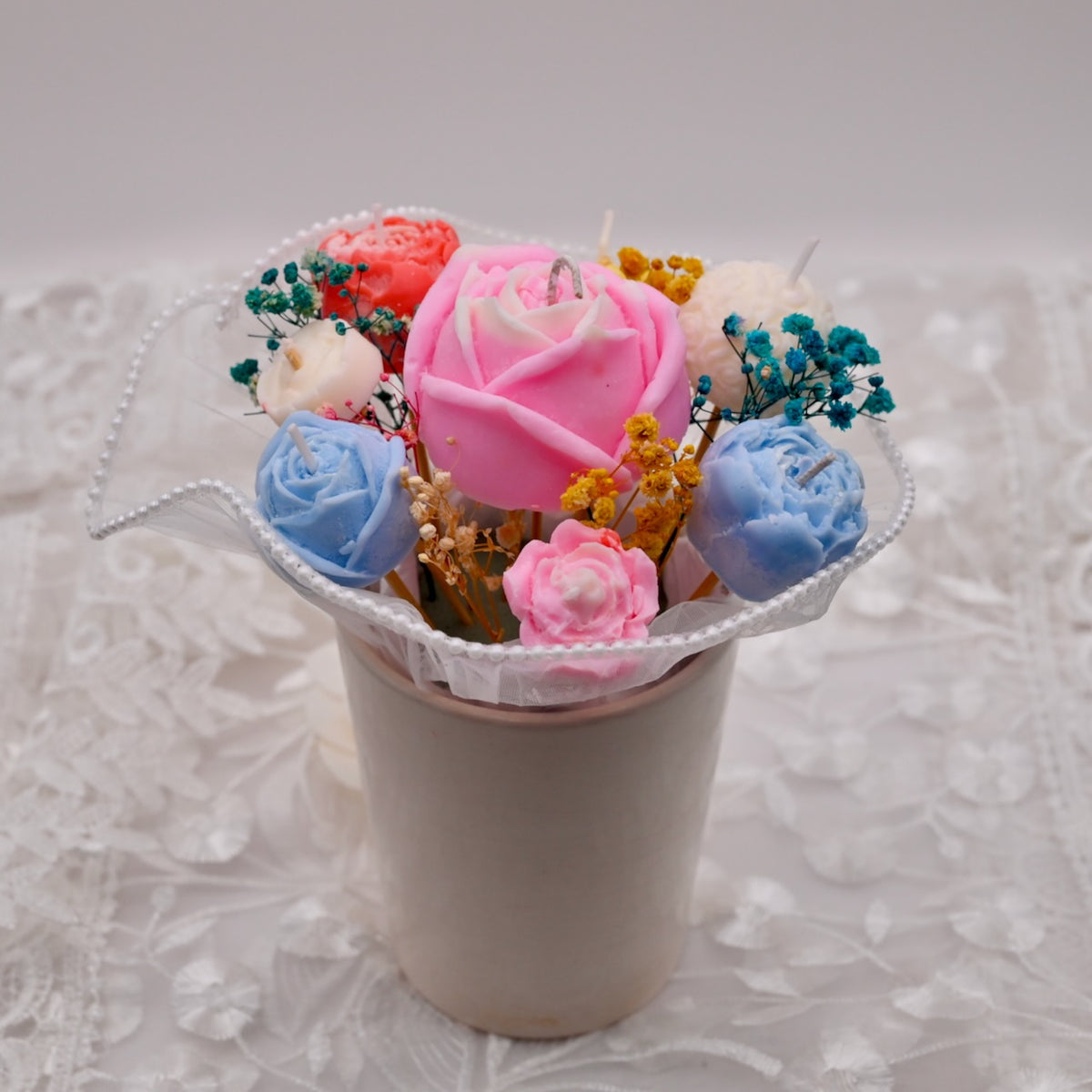 Bouquet of colorful soy wax flower candles in a white container on a textured gray background