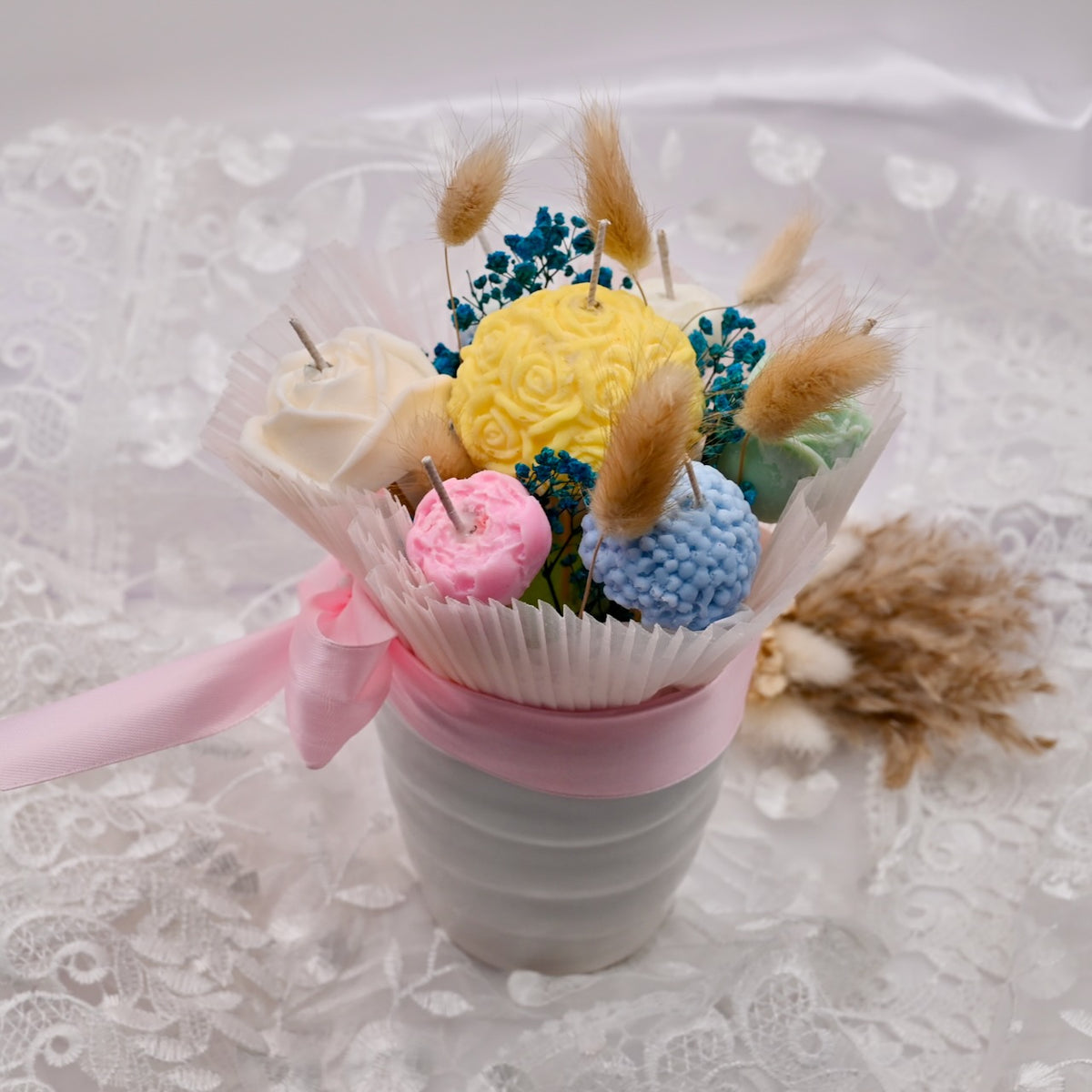 Bouquet of colorful soy wax flower candles in a small pot on a lace tablecloth