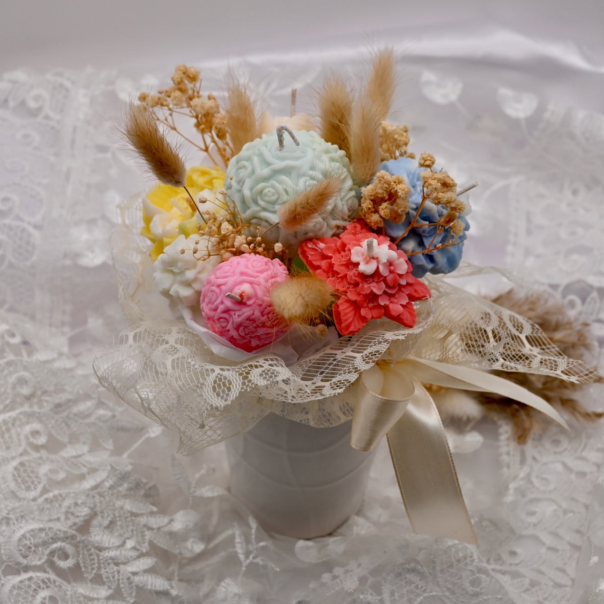 Colorful soy wax flower candle arrangement with dried decorative accents on a lace background