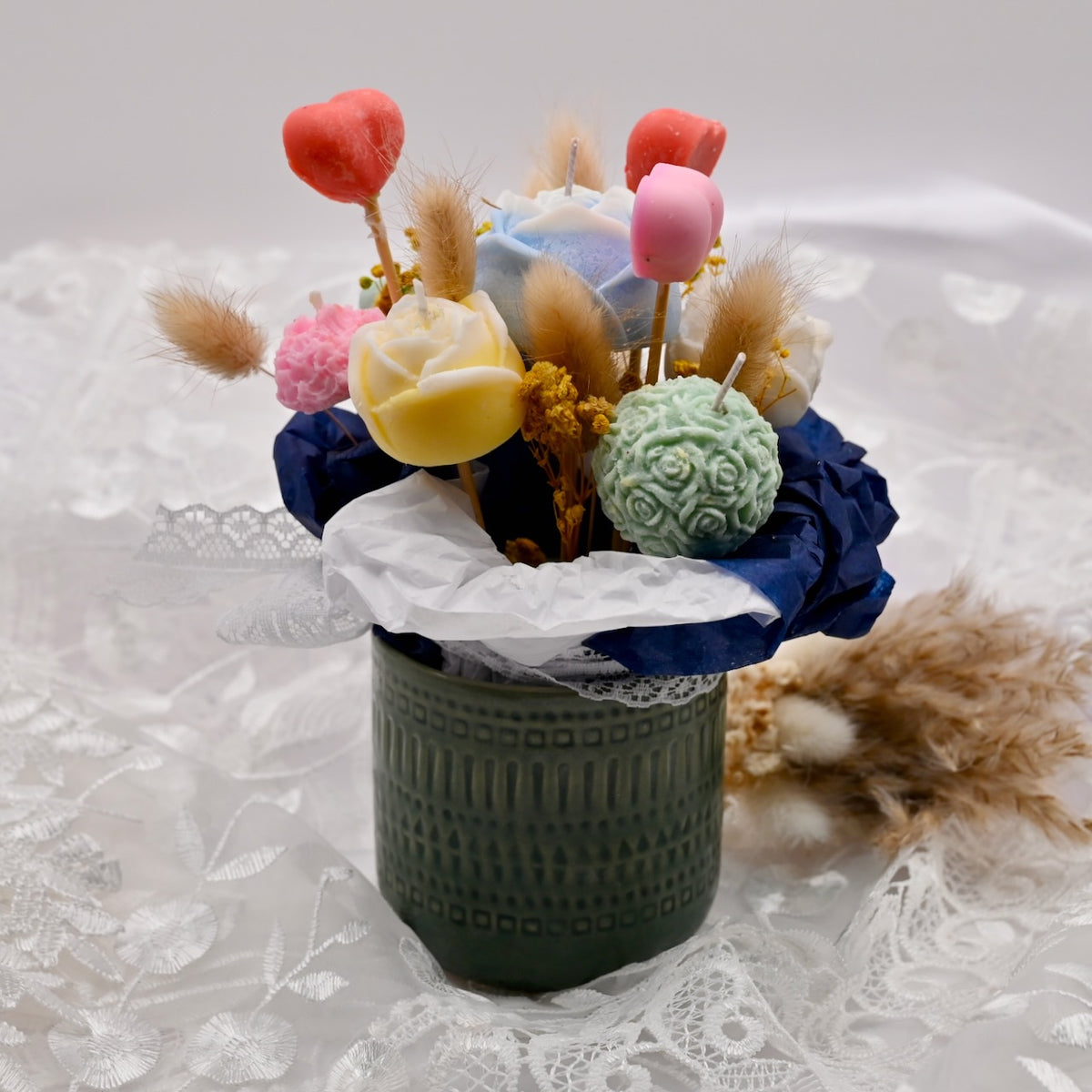 Bouquet of decorative soy wax flower candles in a black holder on a lace background