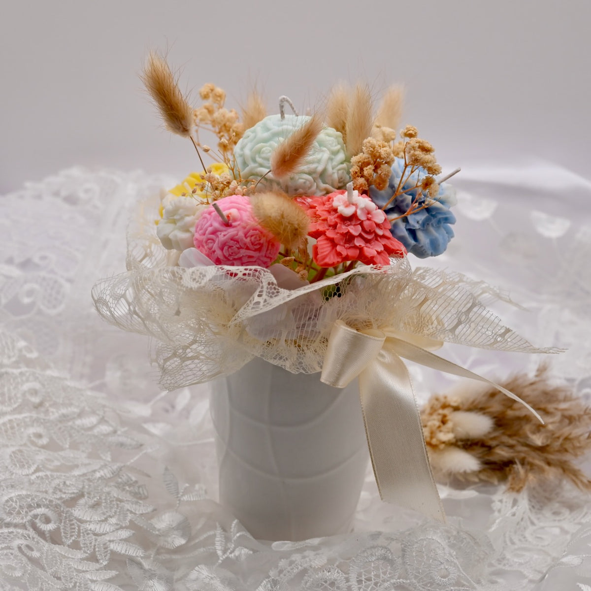 Soy wax flower candle bouquet in a white vase on a lace surface