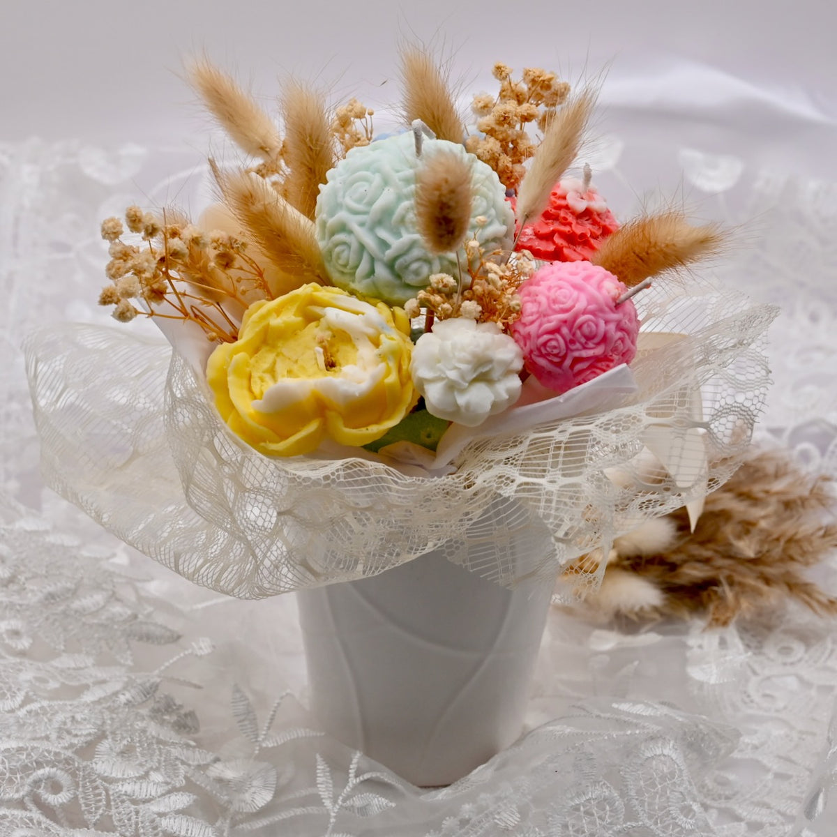 Bouquet of colorful textured soy wax flower candles with dried decorative accents on a lace background
