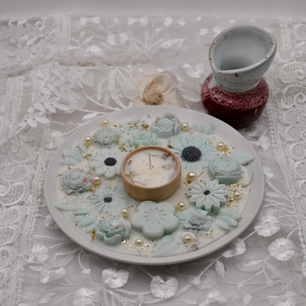 Decorative plate with floral designs, a candle, and small decorative items on a lace tablecloth.  Diwali decorative plate.