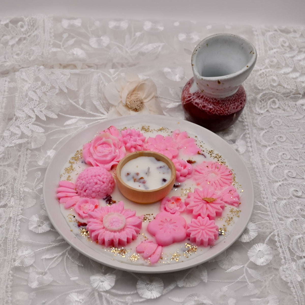 Decorative plate with a pink floral soy wax candle and a small bowl on a lace tablecloth.  Diwali decorative plate.