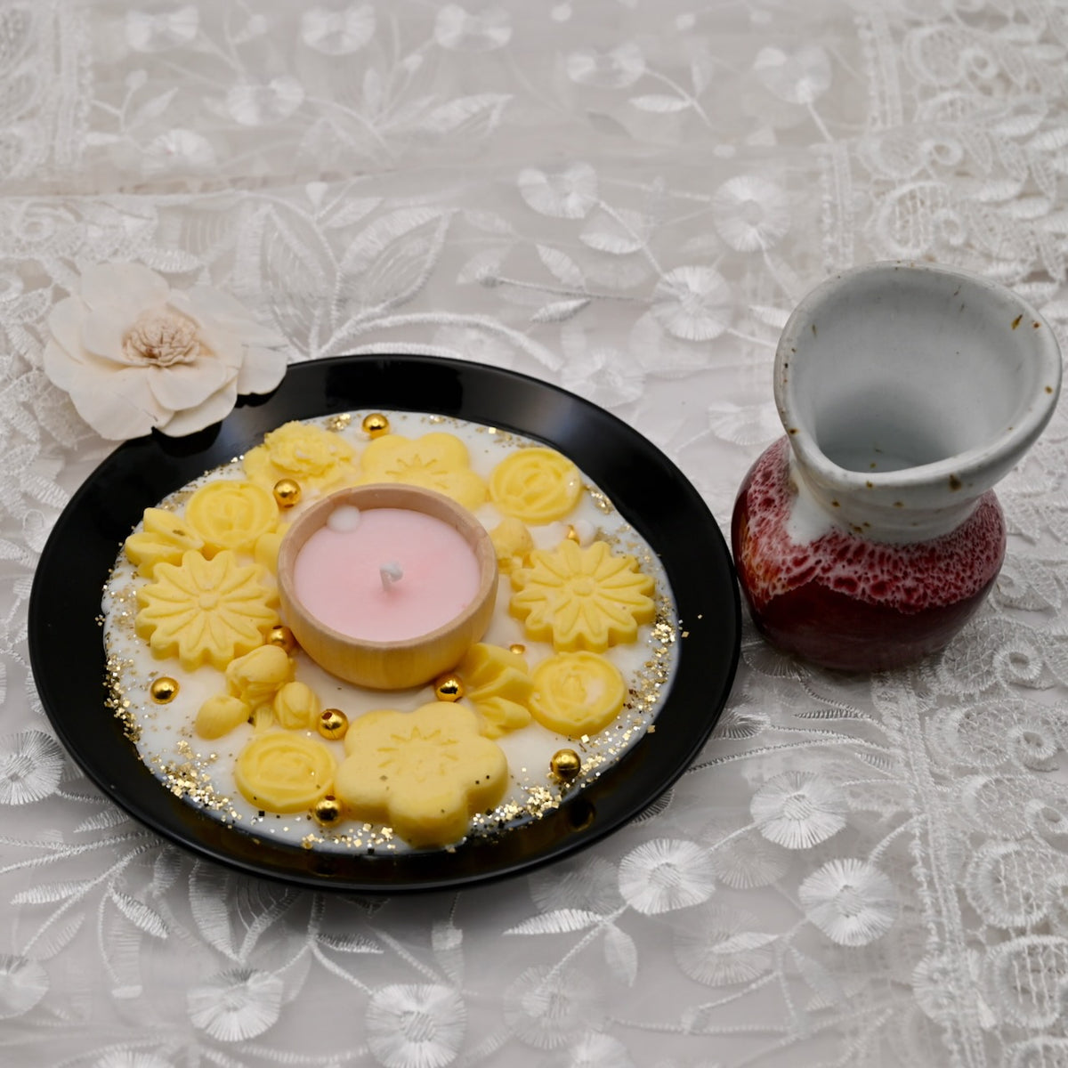 Decorative plate with yellow floral designs and a pink candle, next to a small pitcher on a textured surface.  Diwali decorative plate.