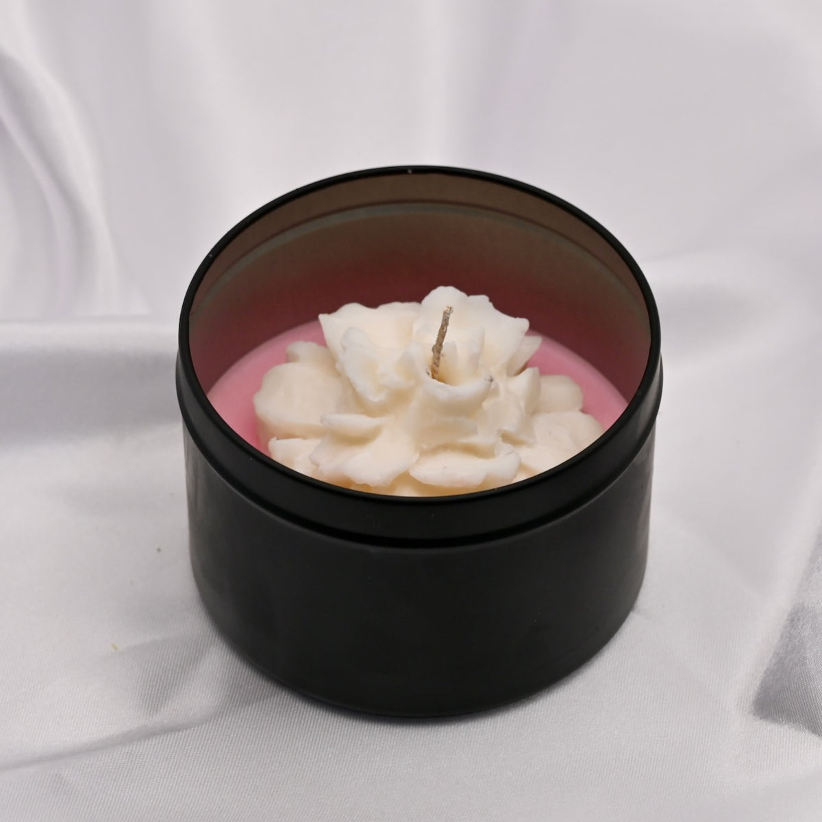 Black container with a white floral candle on a light gray background