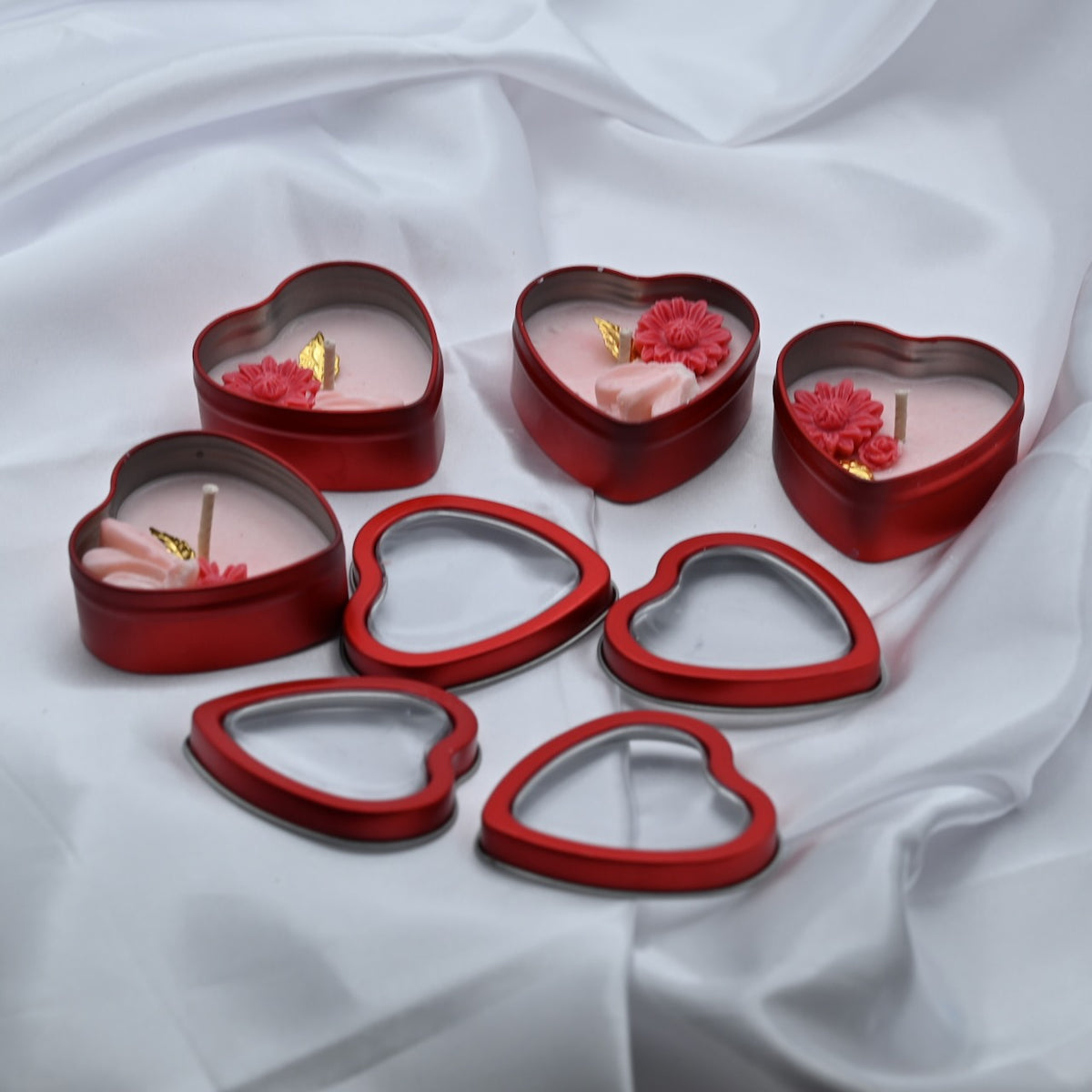 Four open Love Spark mini soy wax candles in red heart-shaped tins with pink floral wax decorations and their window lids displayed in front.