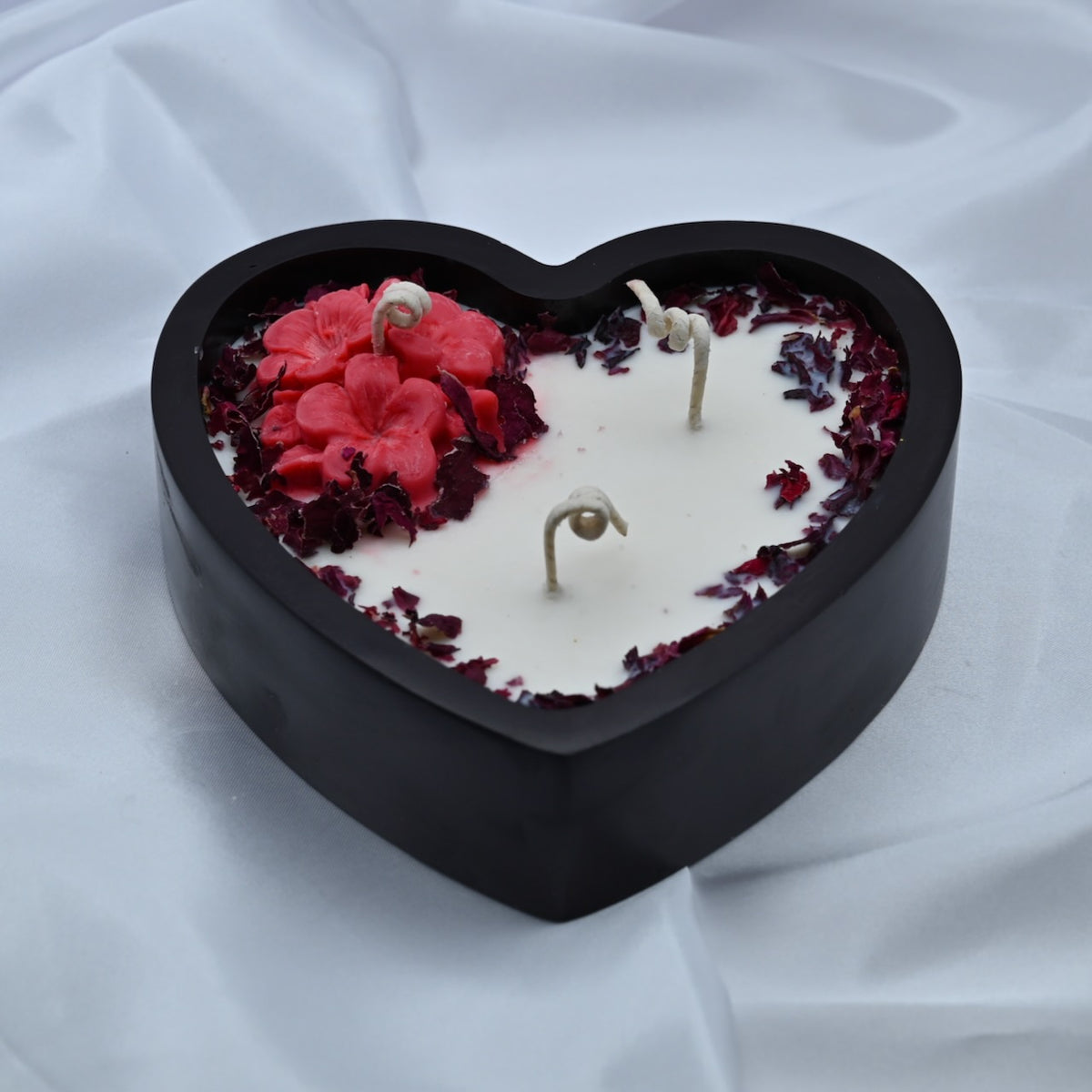 Blushing Heart soy wax candle in a black heart-shaped wooden container with red wax flowers, dried rose petals, and three wicks.