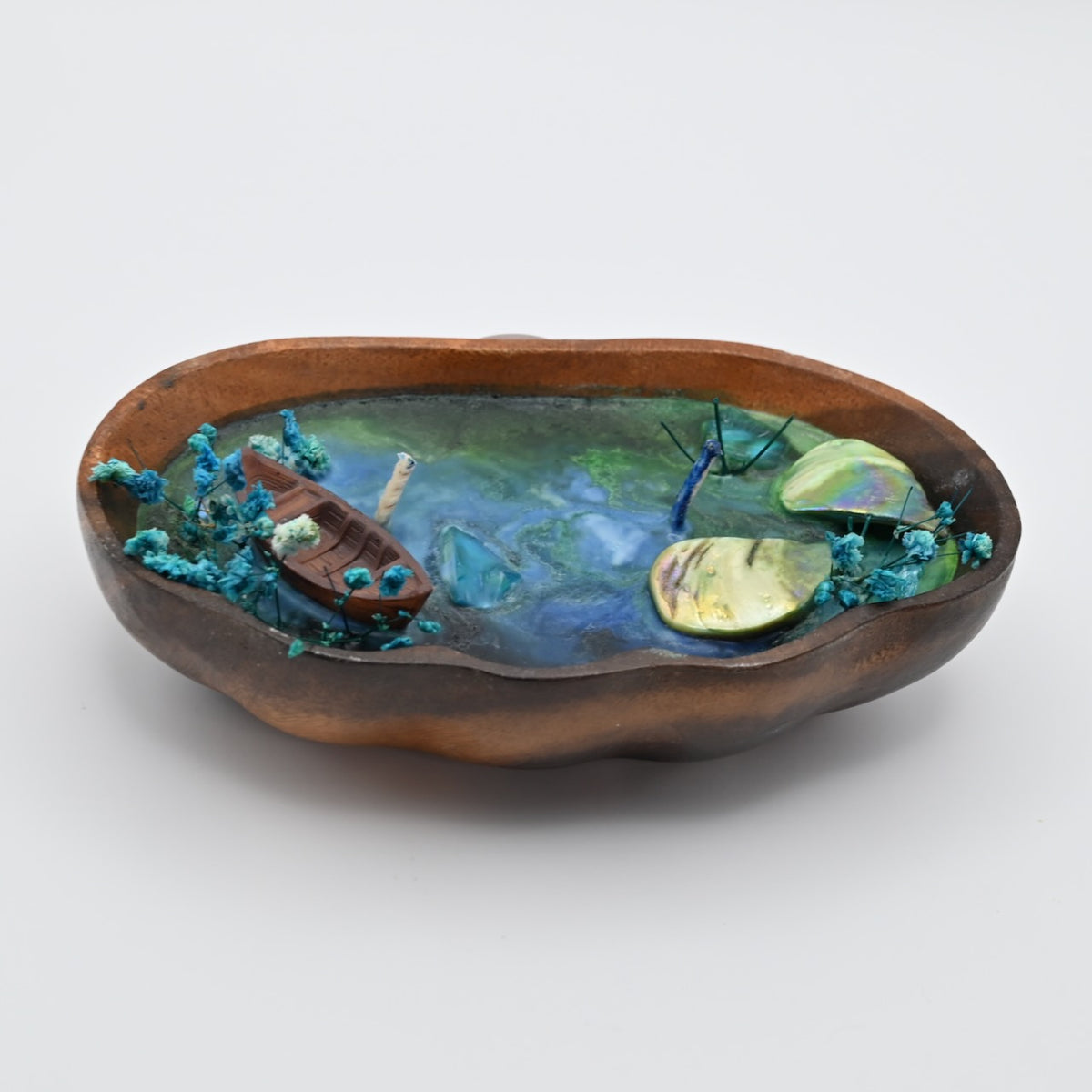 Left-angled view of the Whispering Sandal ocean bloom soy wax candle in a handcrafted wooden tray with a boat, shell accents, and dried blue flowers.