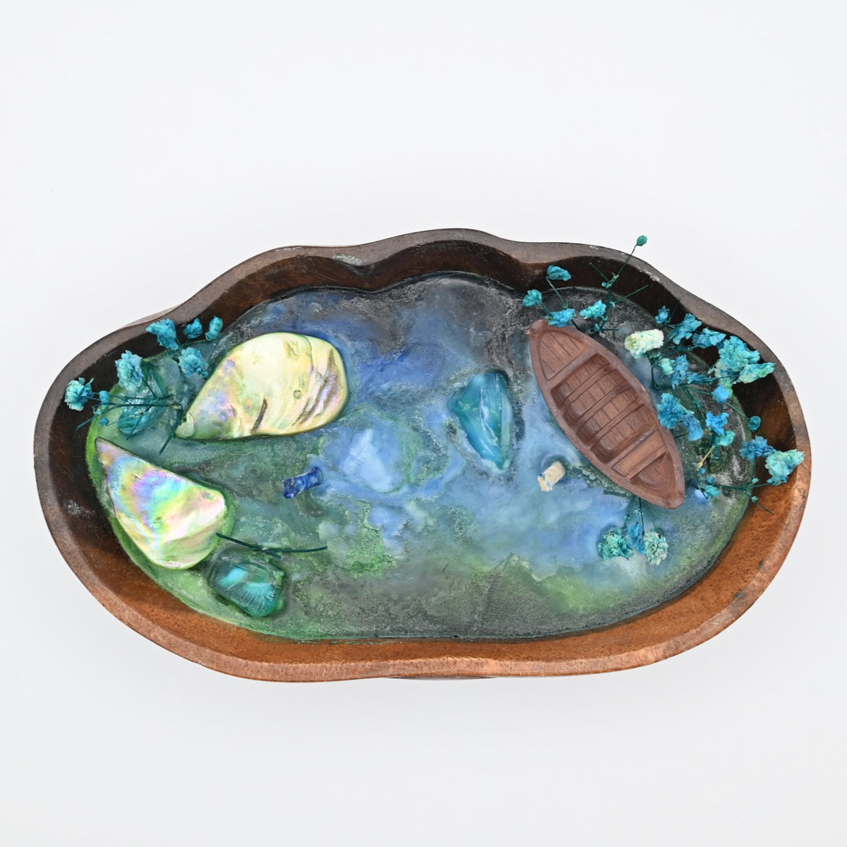 Top view of the Whispering Sandal ocean bloom soy wax candle in a handcrafted wooden tray with a wooden boat, shell accents, and dried blue flowers.