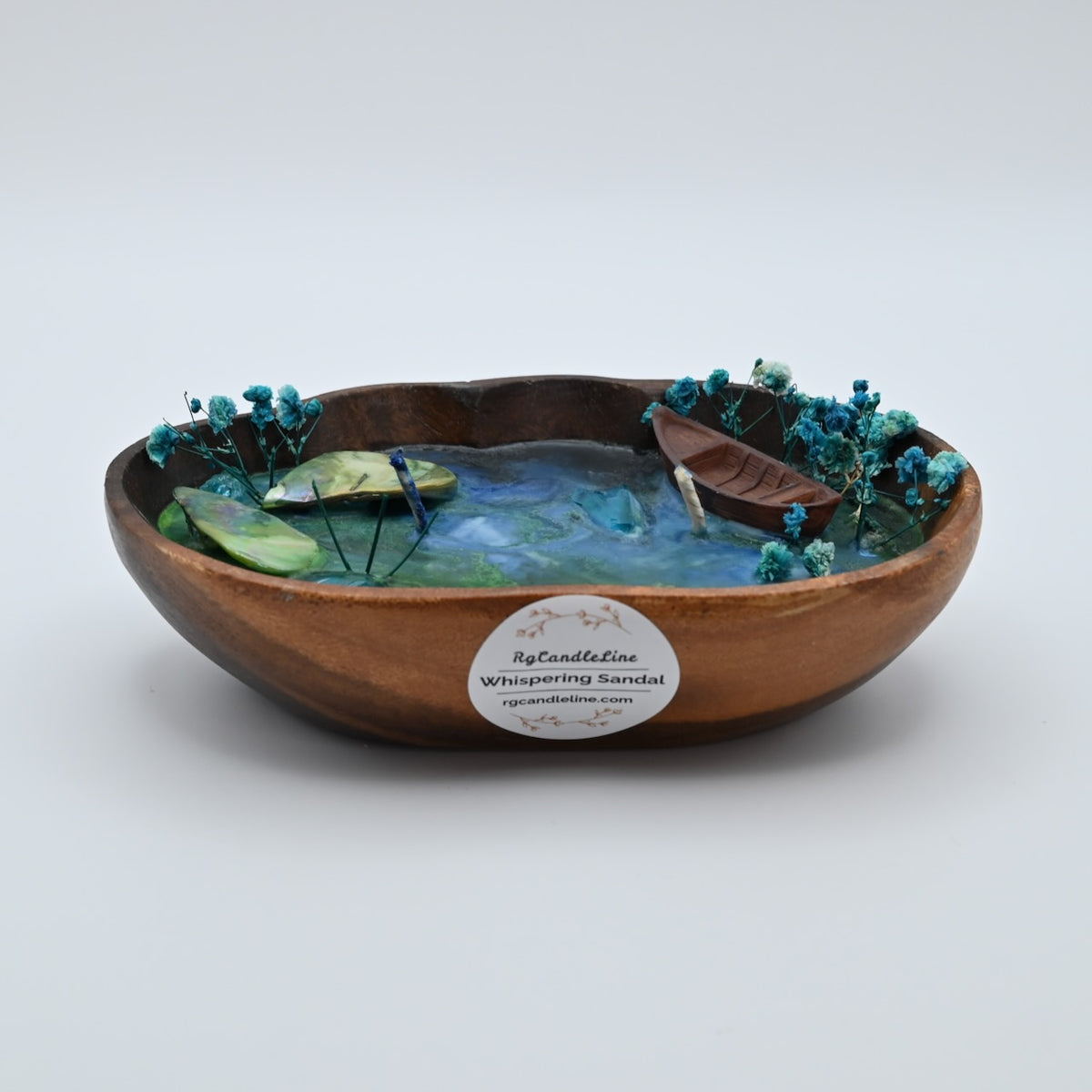 Ocean Bloom soy candle in a square wooden bowl with blue wax, shell accents, dried flowers, and boat detail