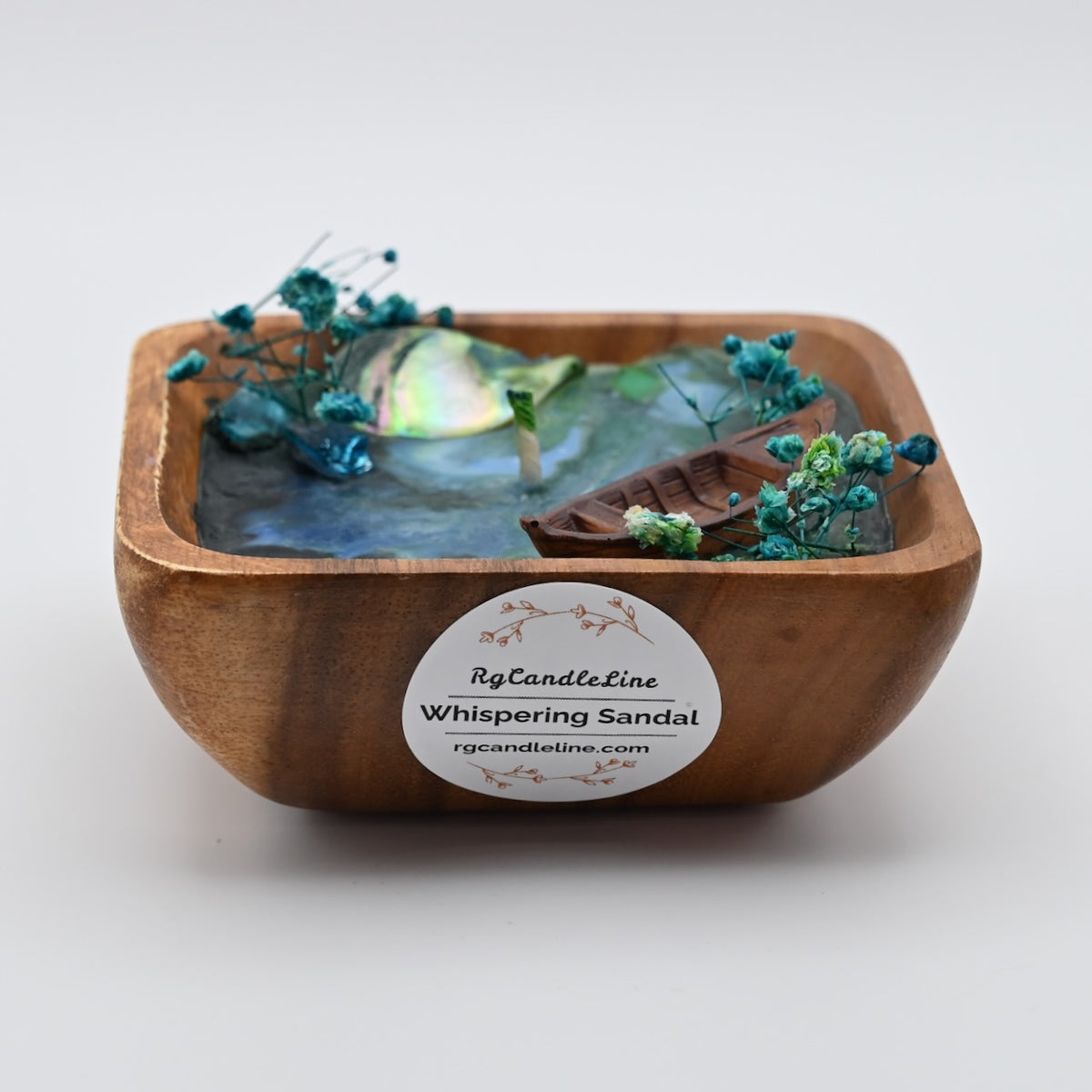 Front view of wooden bowl candle with blue wax, shell accents, dried flowers, and boat detail