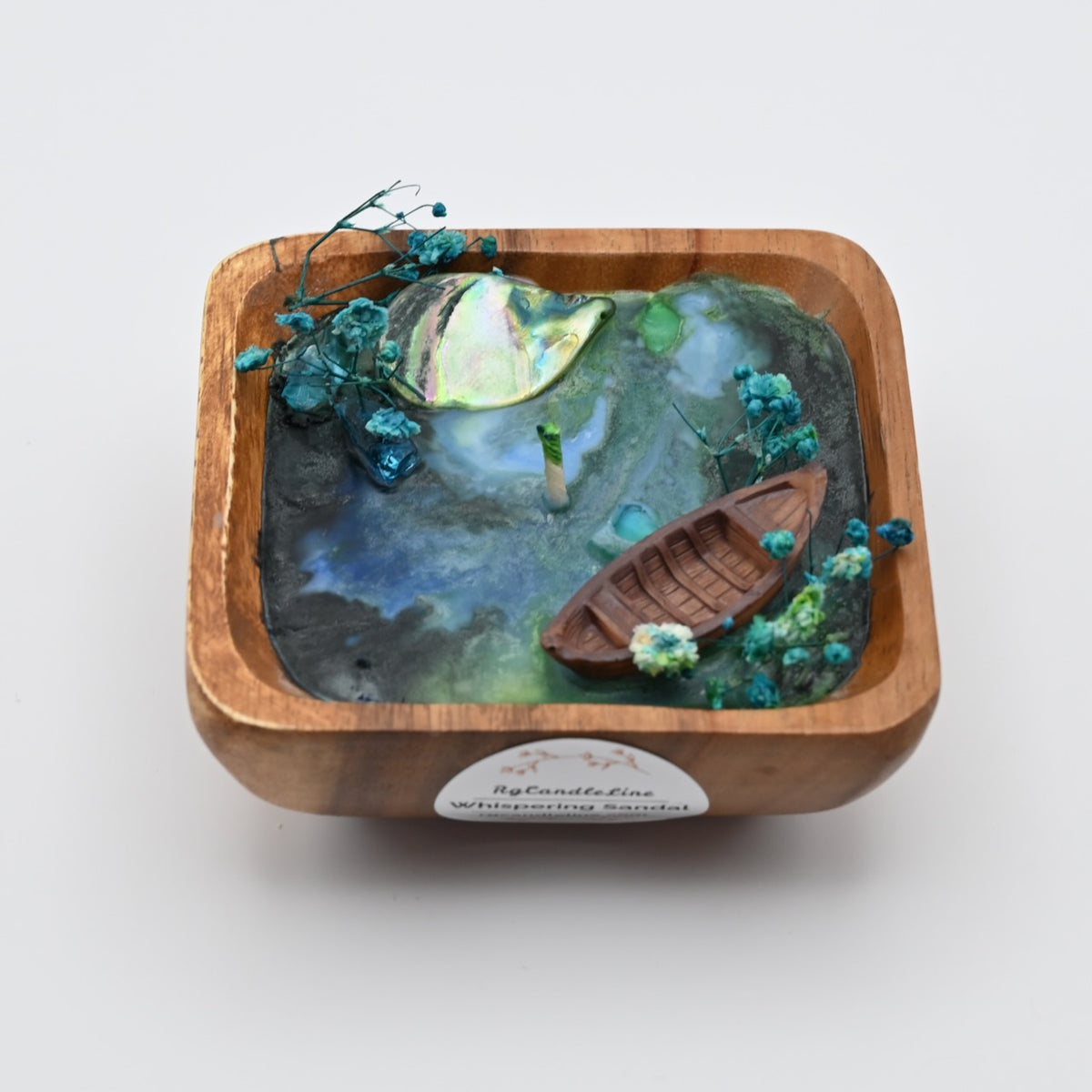 Top view of wooden bowl candle with blue wax, shell accents, dried flowers, and boat detail