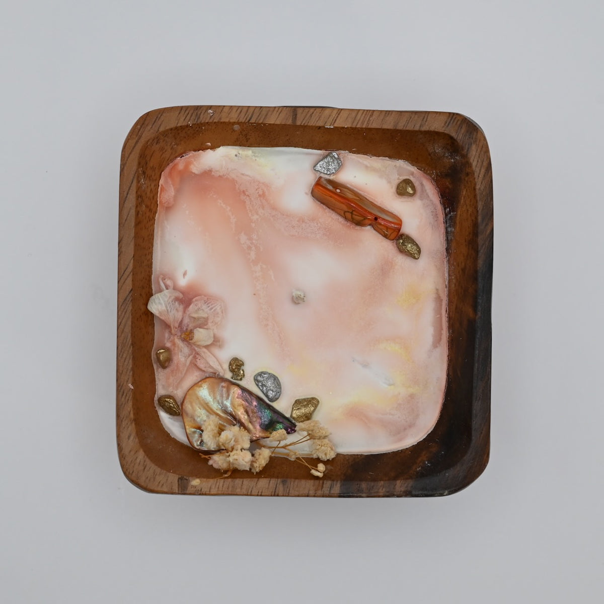 Top view of wooden bowl candle with pink wax, shell, crystal, and dried flower accents