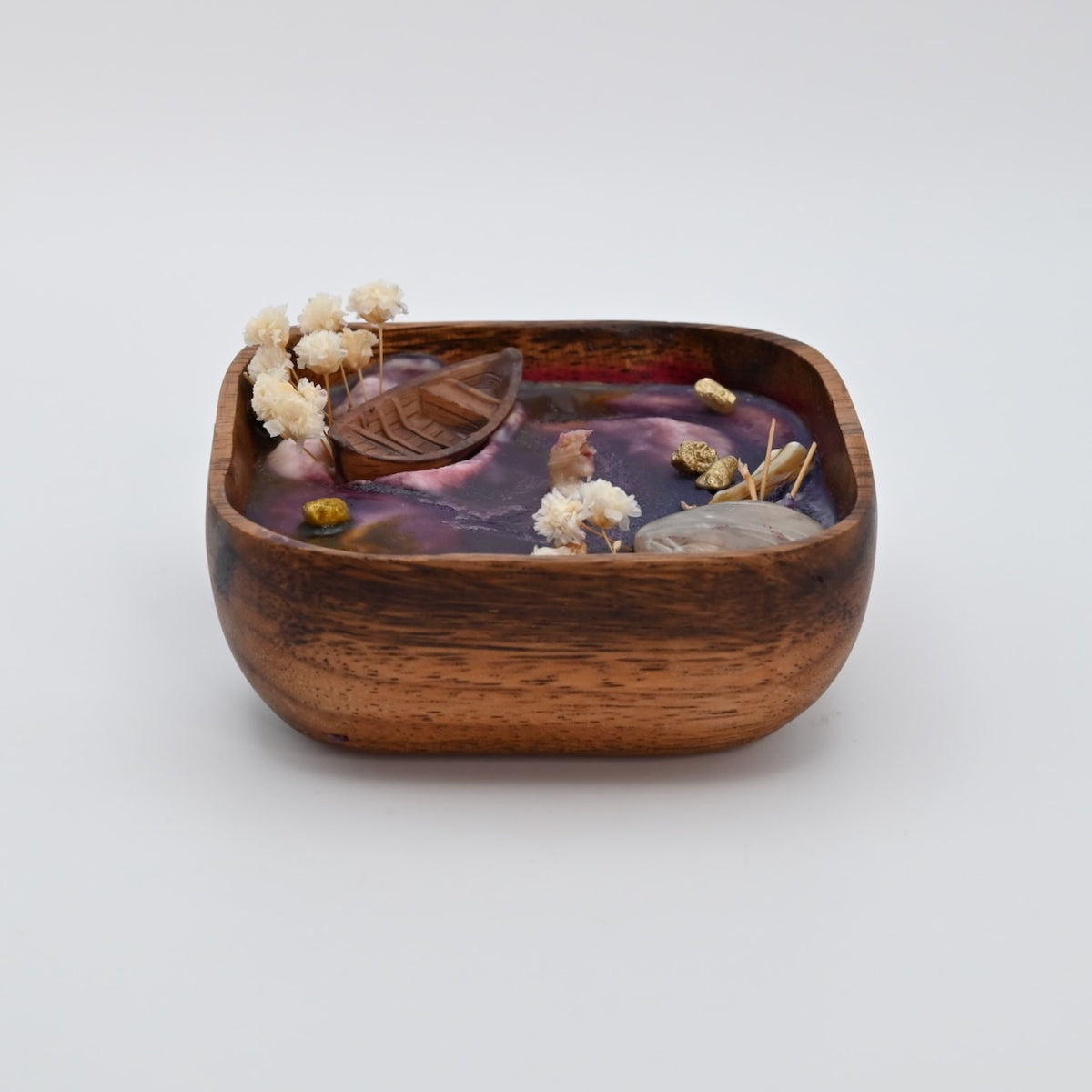 Front view of the Ocean Bloom wooden bowl candle with purple wax, shell accents, dried flowers, and a decorative boat detail.