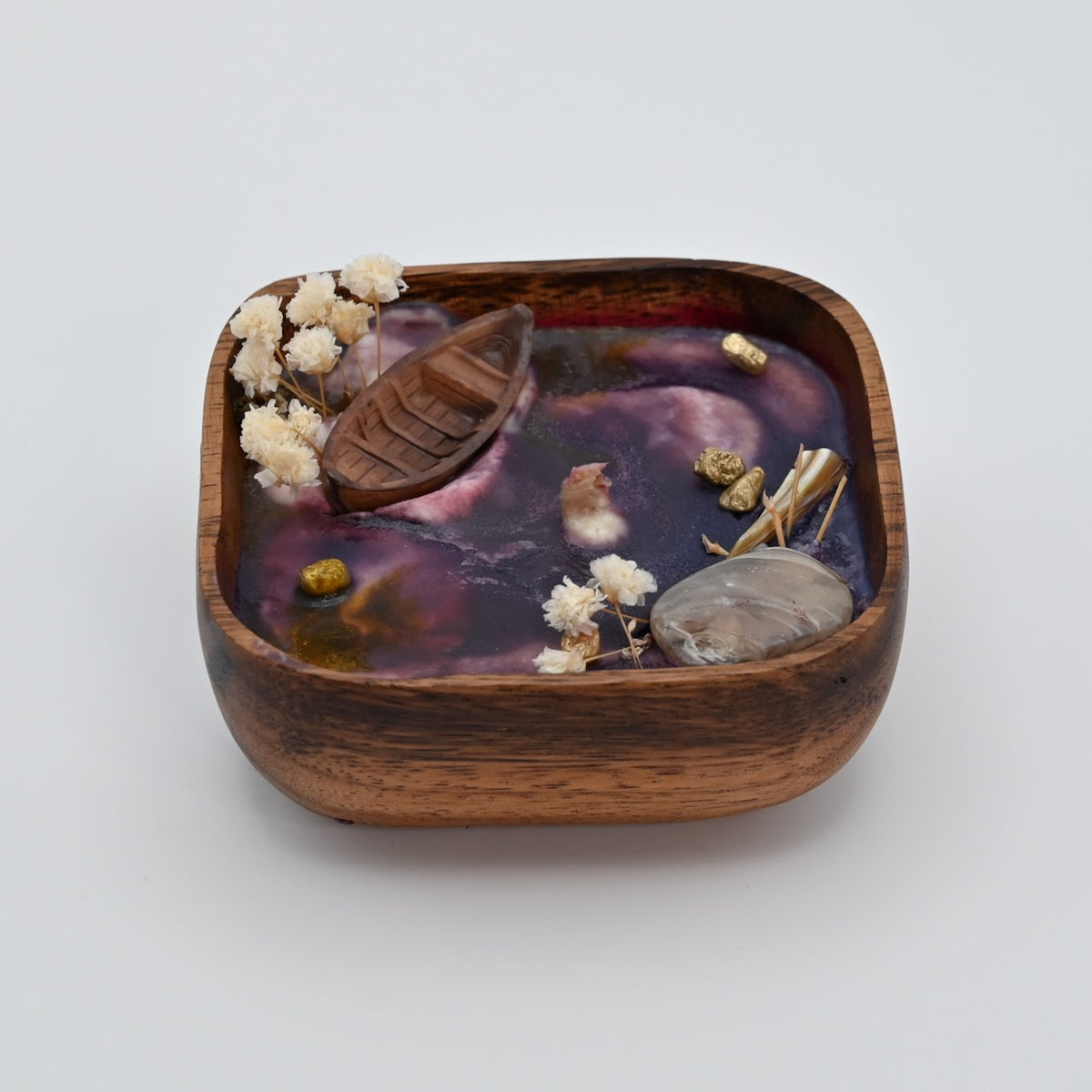 Left view of wooden bowl candle with purple wax, shell accents, dried flowers, and boat detail