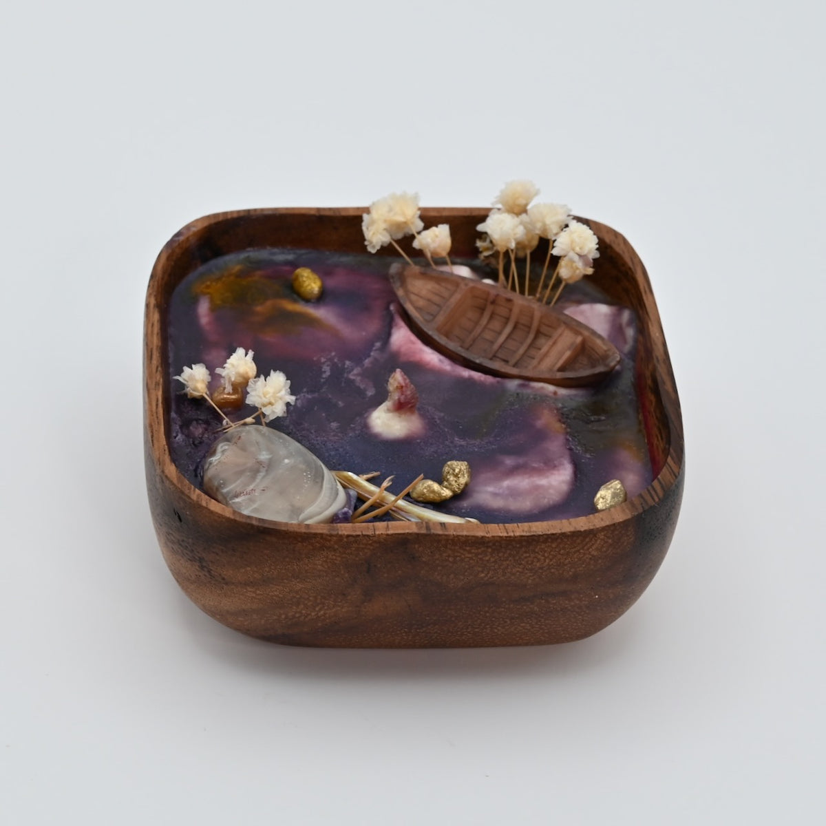 Right view of wooden bowl candle with purple wax, shell accents, dried flowers, and boat detail