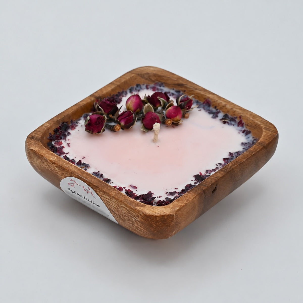 Left view of a 4-inch acacia wood bowl candle with pale wax, dried rosebuds, and a dark floral border.