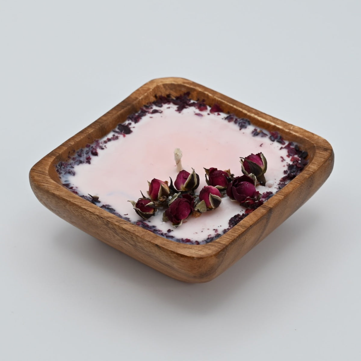 Side view of a 4-inch acacia wood bowl candle with pale wax, dried rosebuds, and a dark floral border.