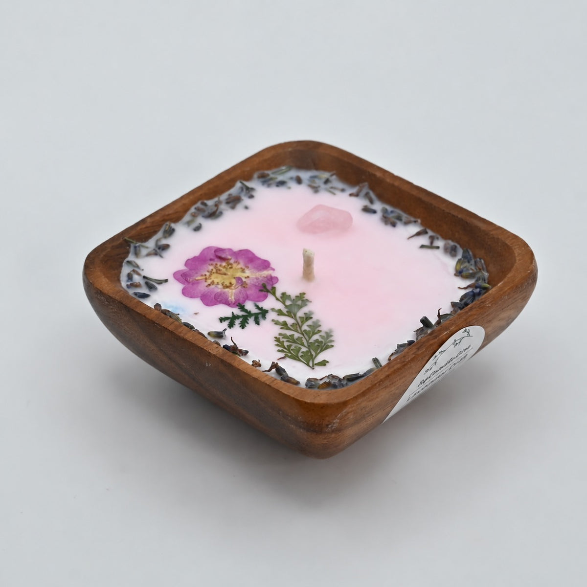 Left view of a 4-inch acacia wood bowl candle with pale wax and pressed purple flowers.